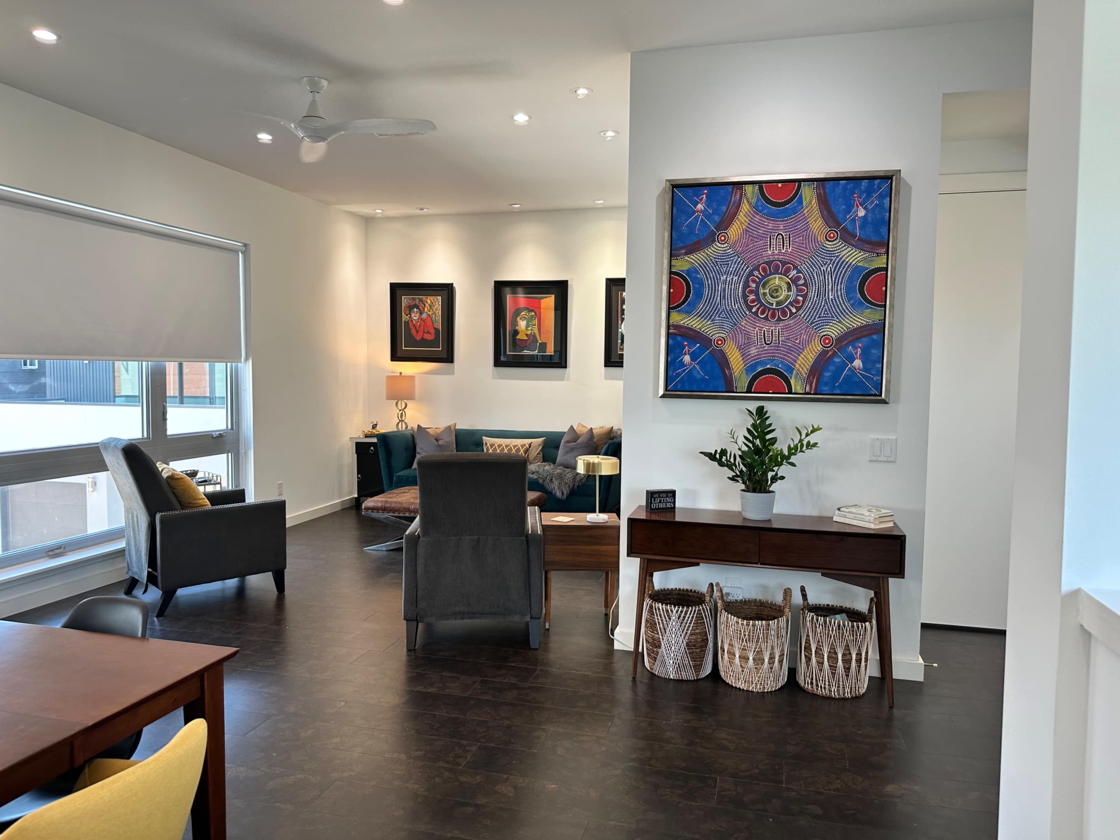 A modern living area featuring a gray sofa, a coffee table with decorative items, and framed artwork on the walls, along with a small table displaying a plant and baskets.