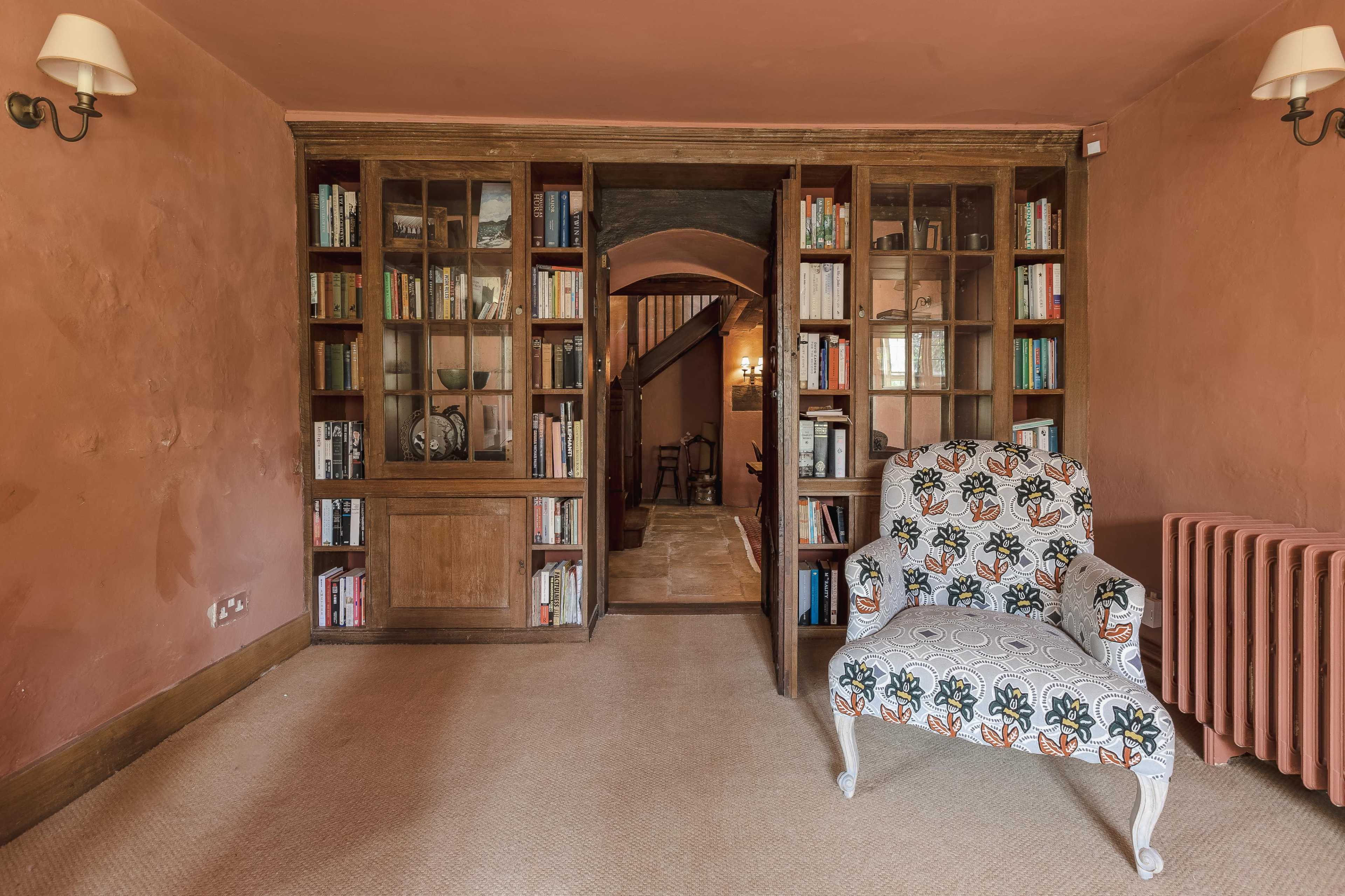 A cozy room with a patterned chair, flanked by bookshelves filled with books, leading to a staircase in the background.