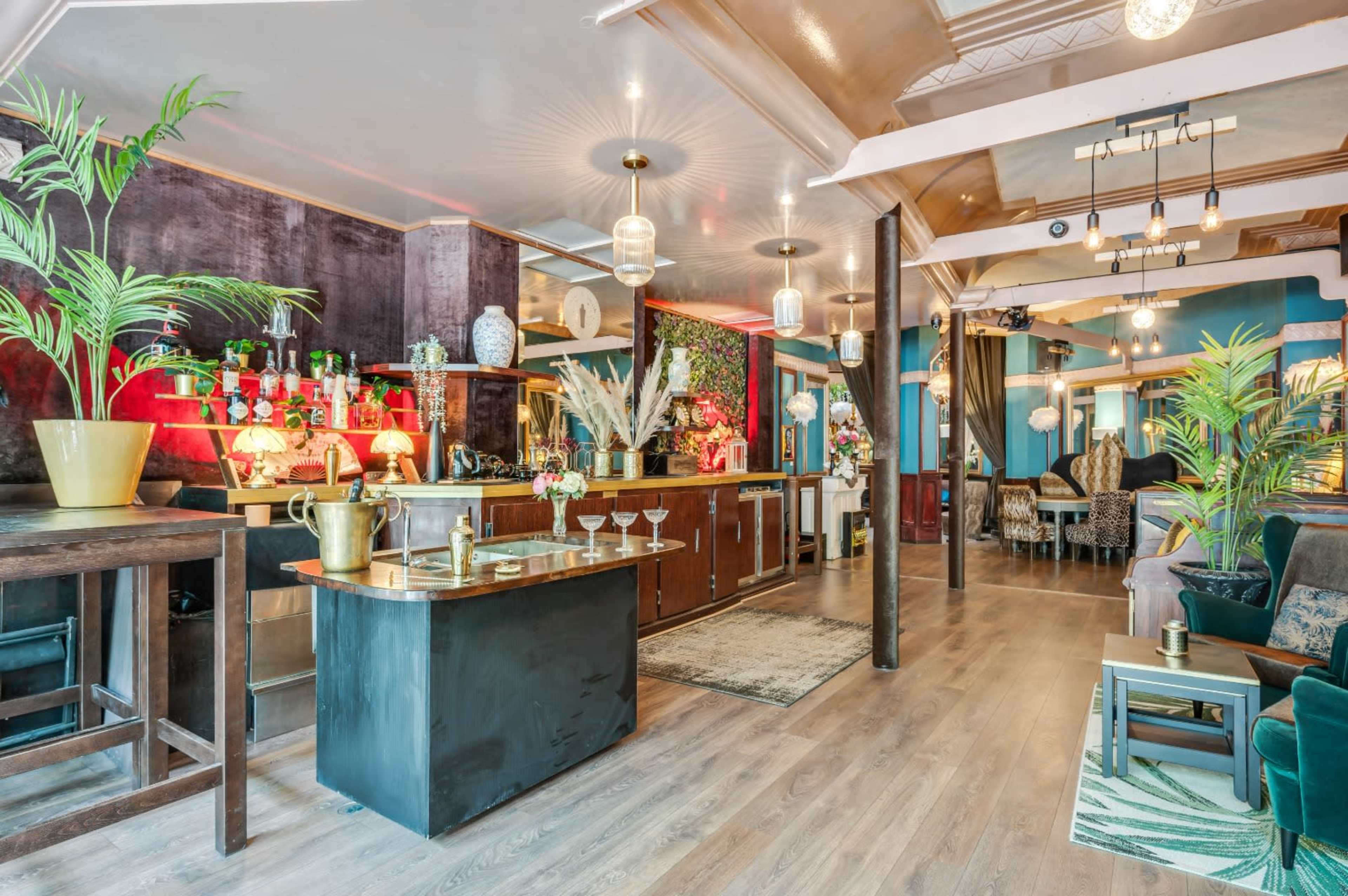 The image shows a stylish bar area with a polished countertop, surrounded by plants and decorative lighting in a modern interior space.