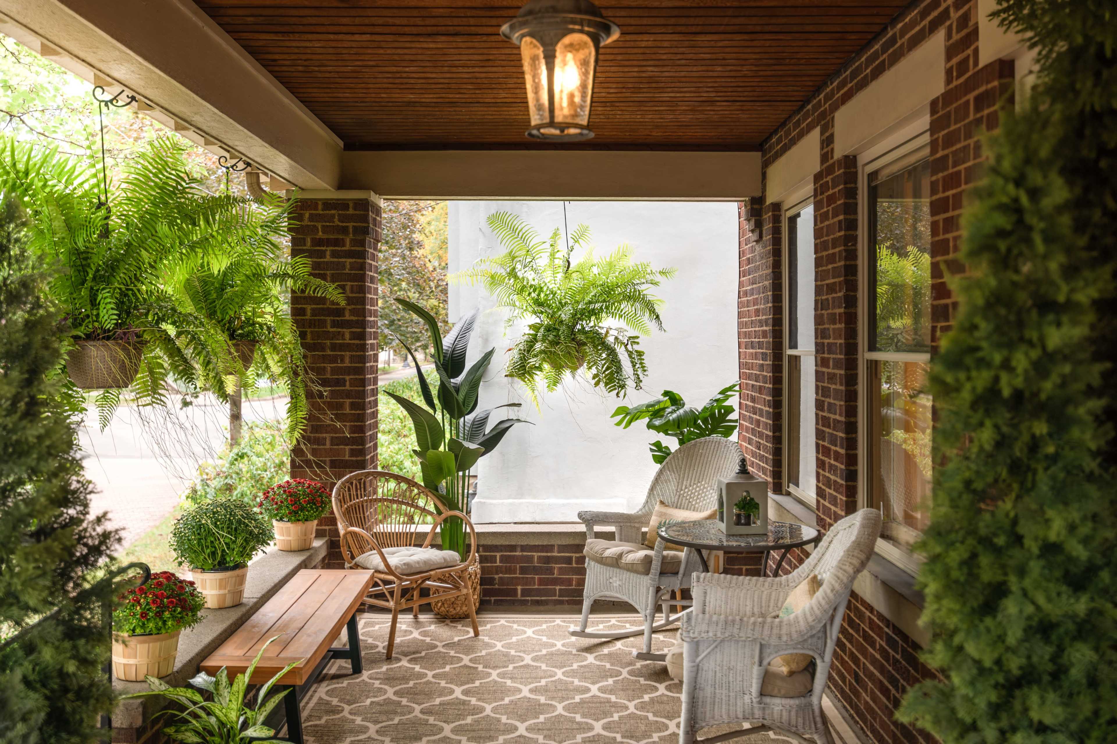 A covered porch with wicker furniture, potted plants, and hanging ferns, creating a cozy outdoor seating area.