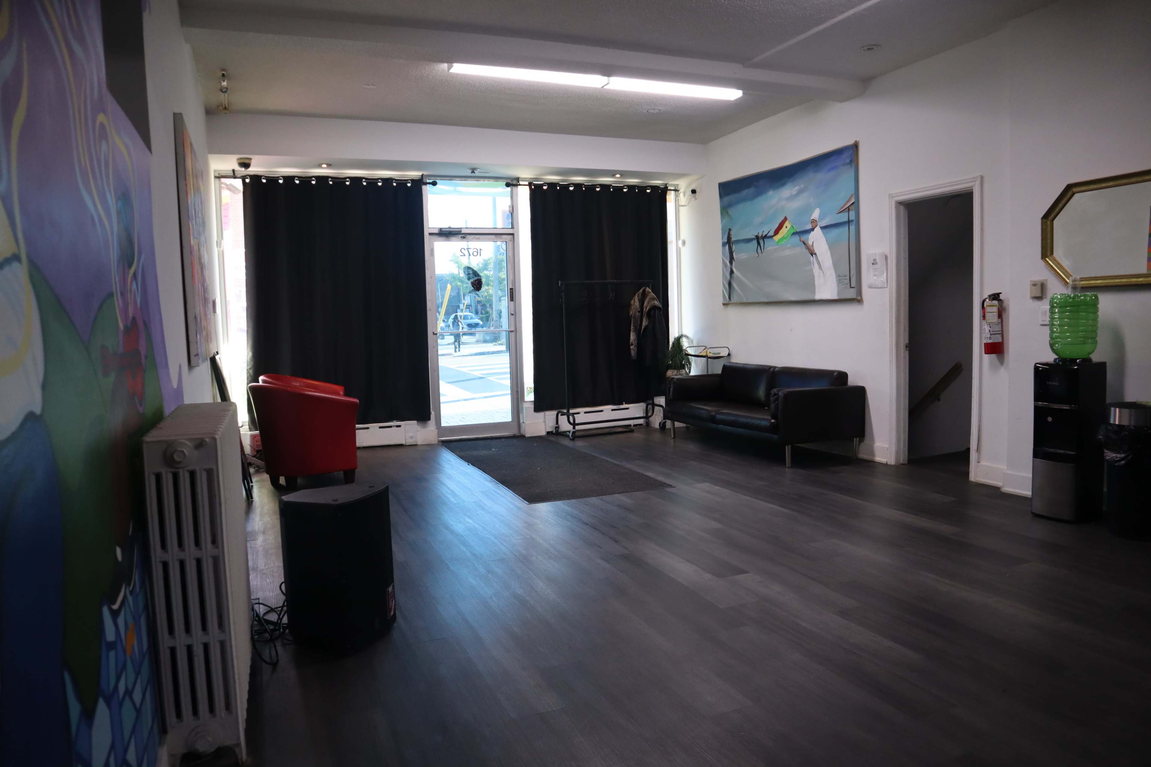 The room features a hardwood floor, a black sofa, a red chair, and a doorway with black curtains leading to the outside.