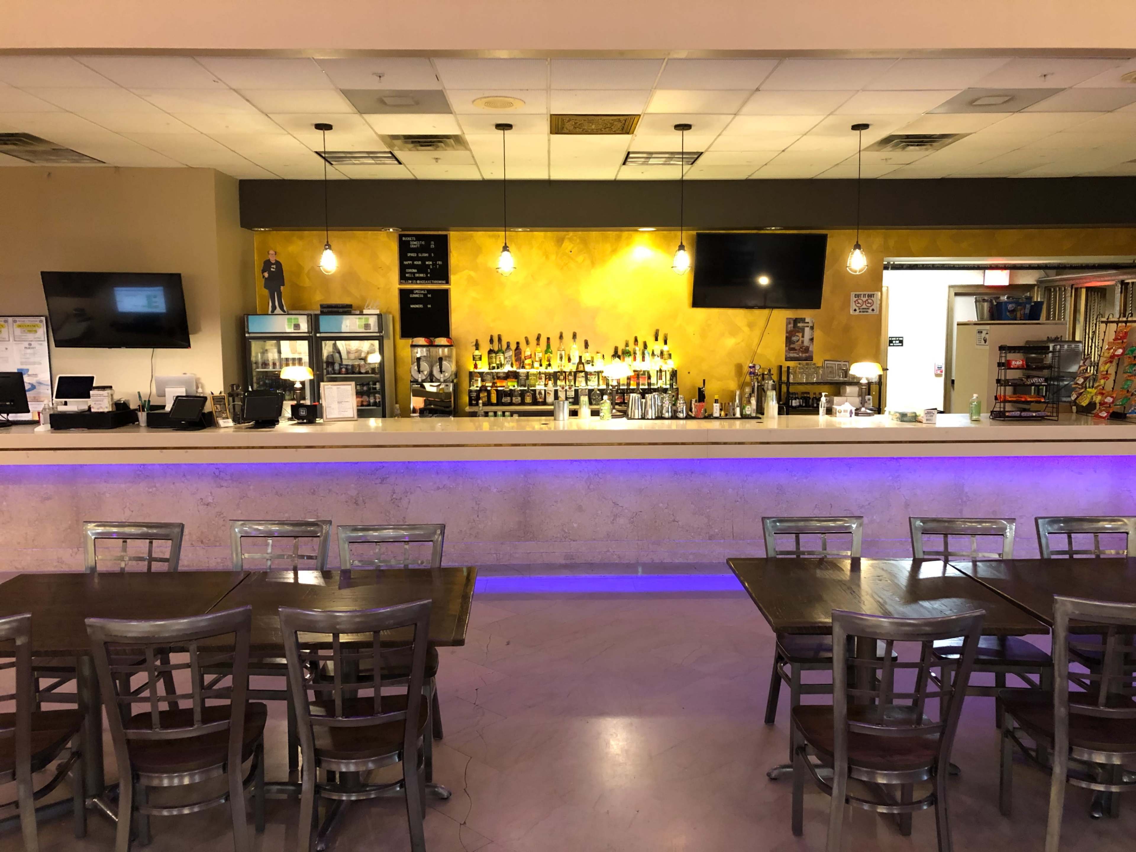 A bar area with a counter, shelves filled with various bottles, and several tables arranged in front of it.