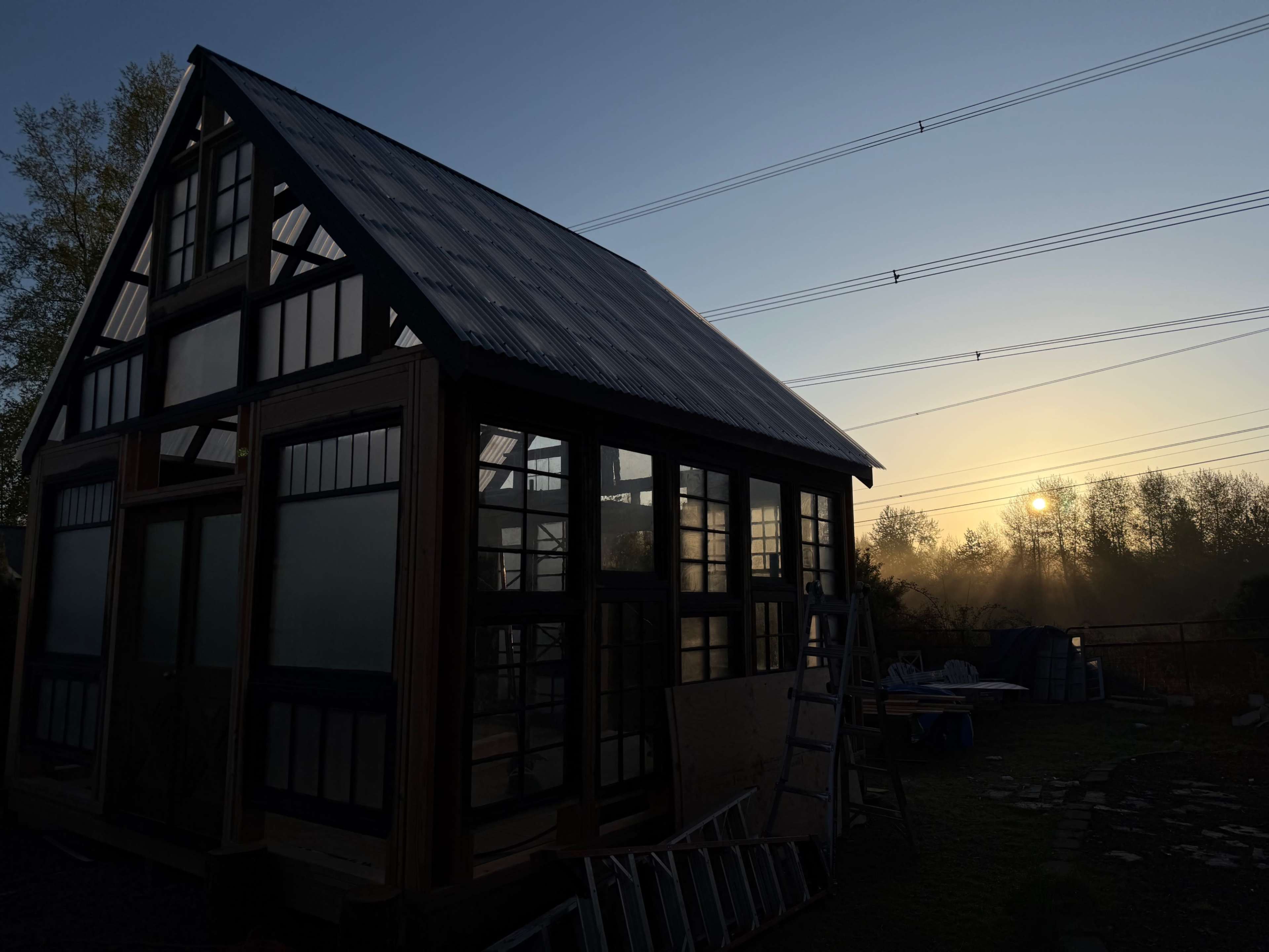 A partially constructed greenhouse stands against a backdrop of a sunrise and misty landscape.