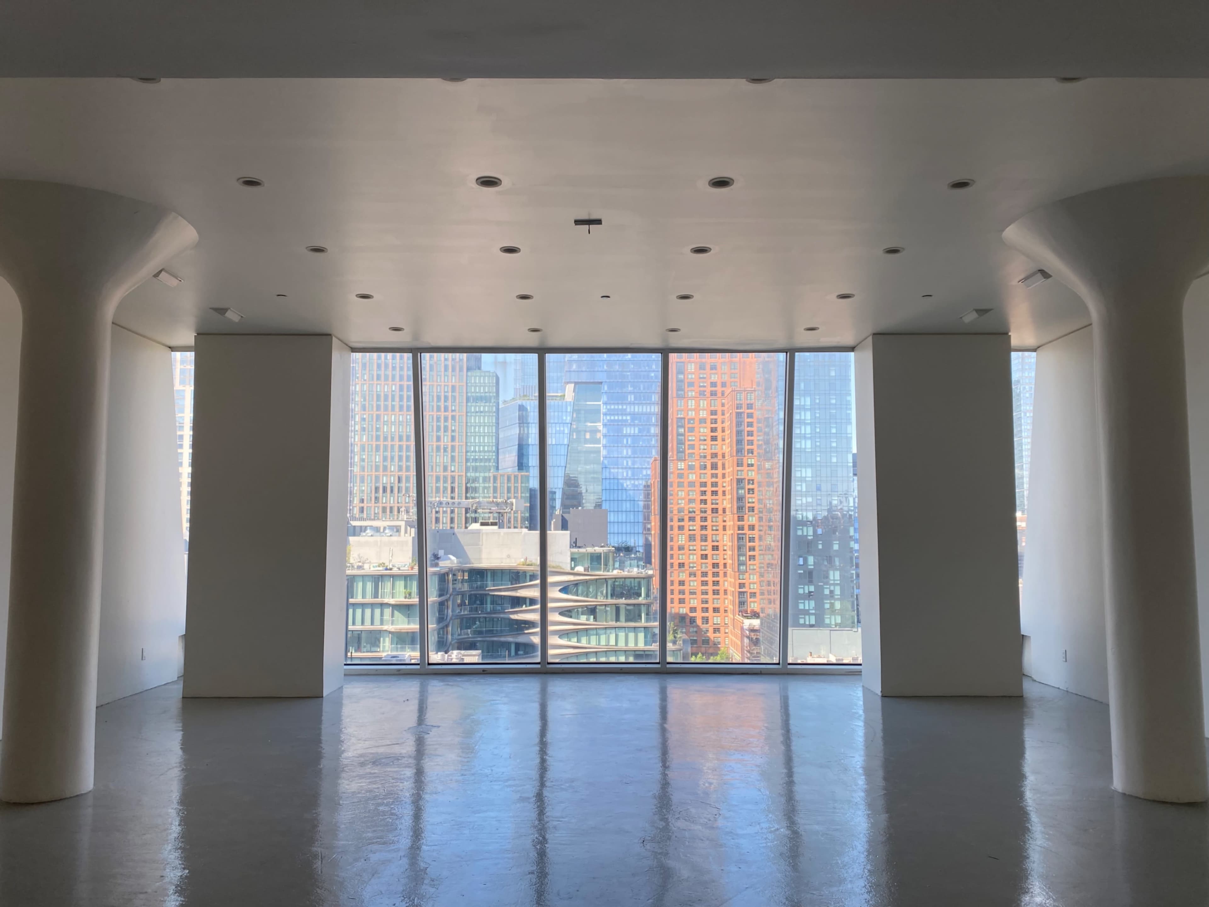 A modern, empty room with large windows offering a view of city skyscrapers and reflections.