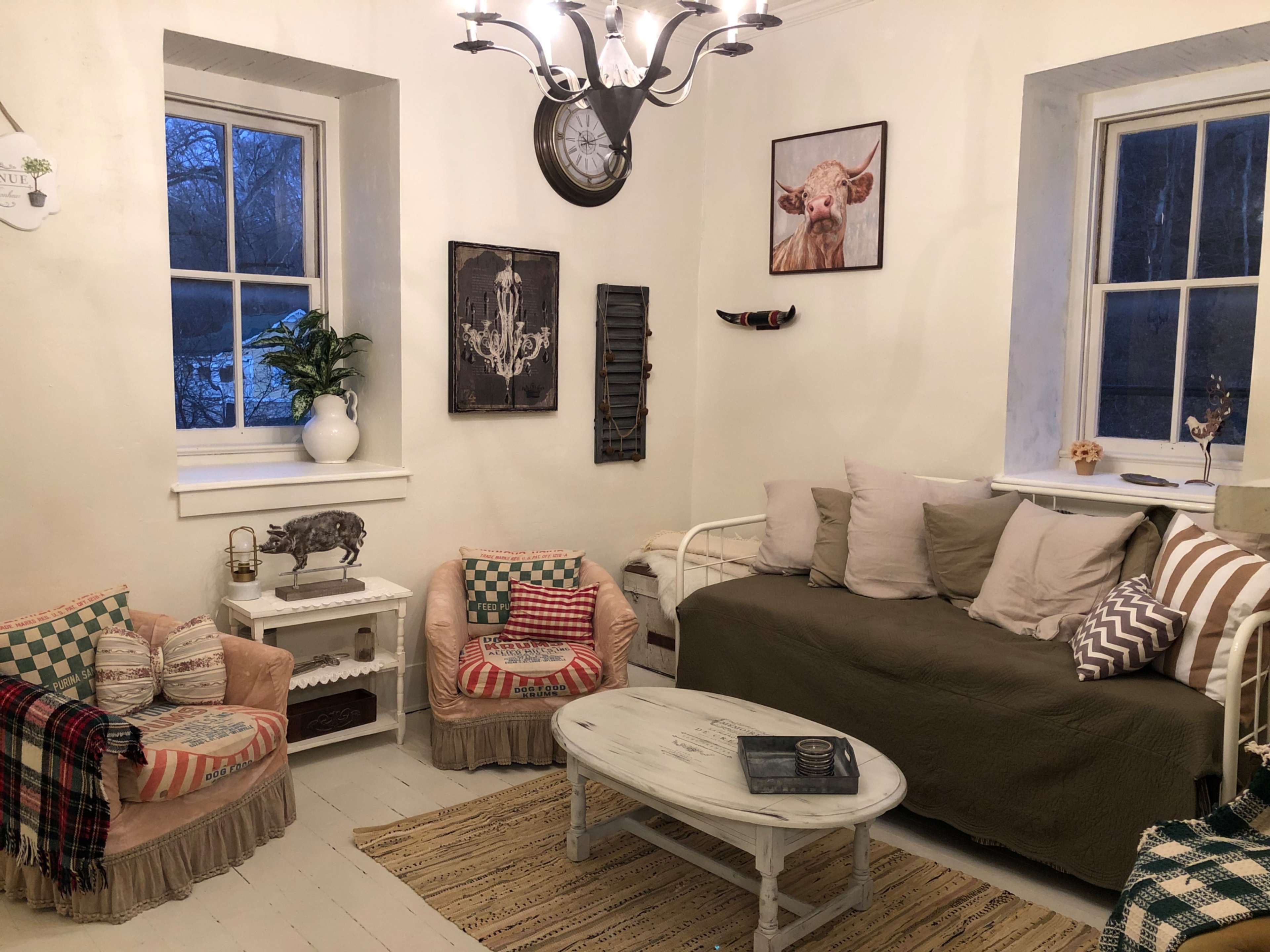 A cozy living room with a sofa, two armchairs, and a coffee table surrounded by light-colored walls and decorative wall art.