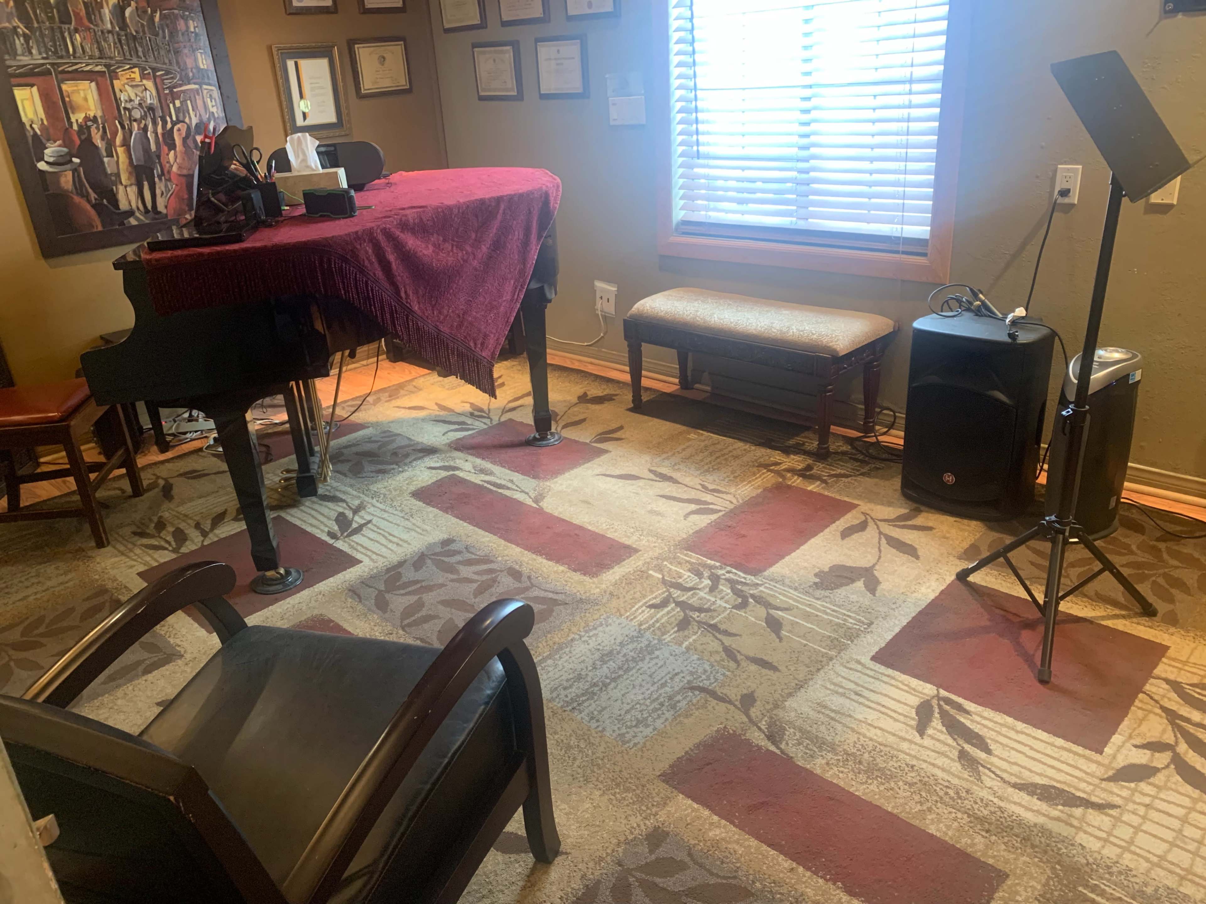 The image shows a room with a piano covered by a red cloth, a chair, a bench, a speaker, and a patterned carpet.