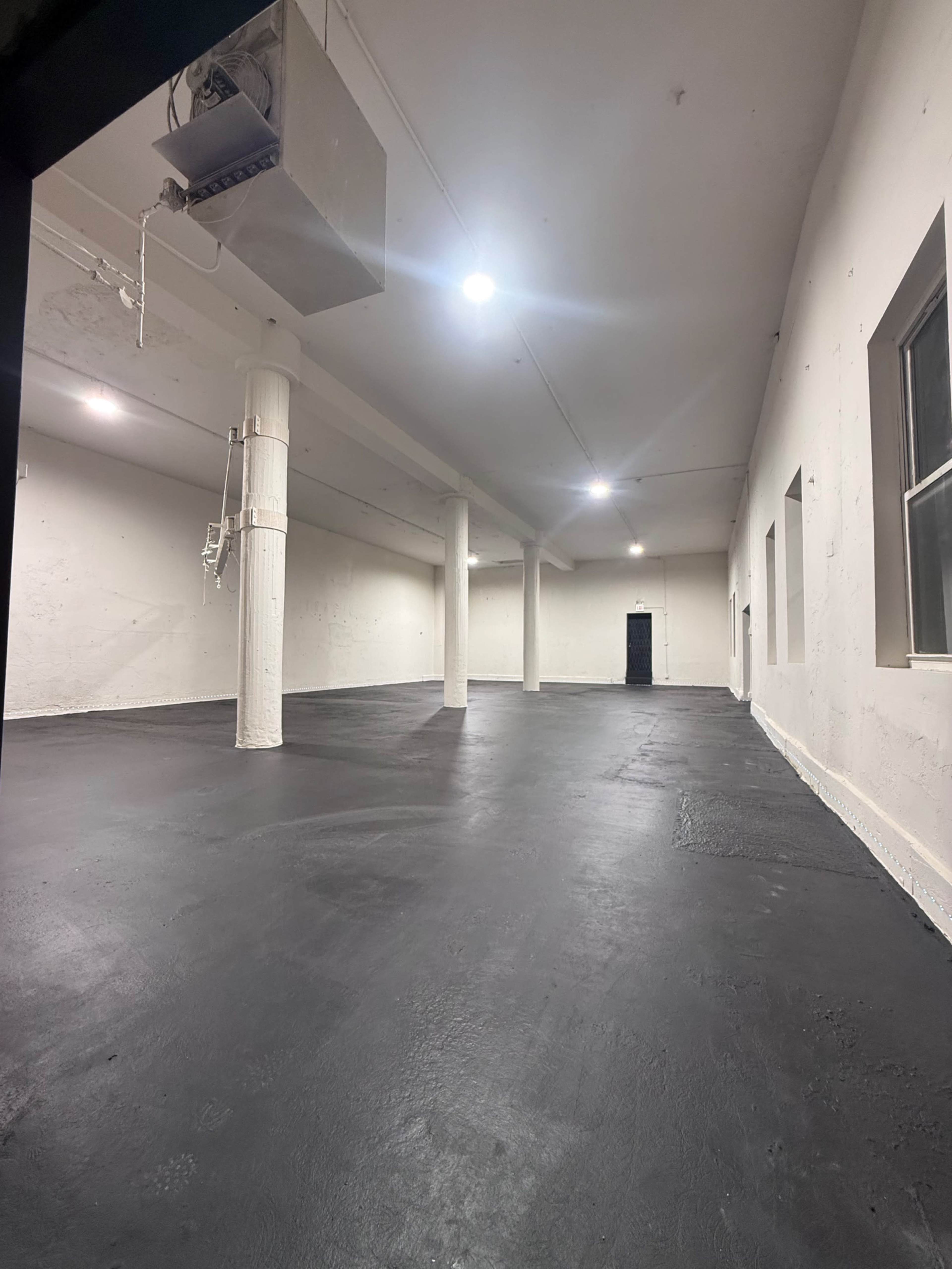 The image shows a spacious, empty room with a black concrete floor and white walls.