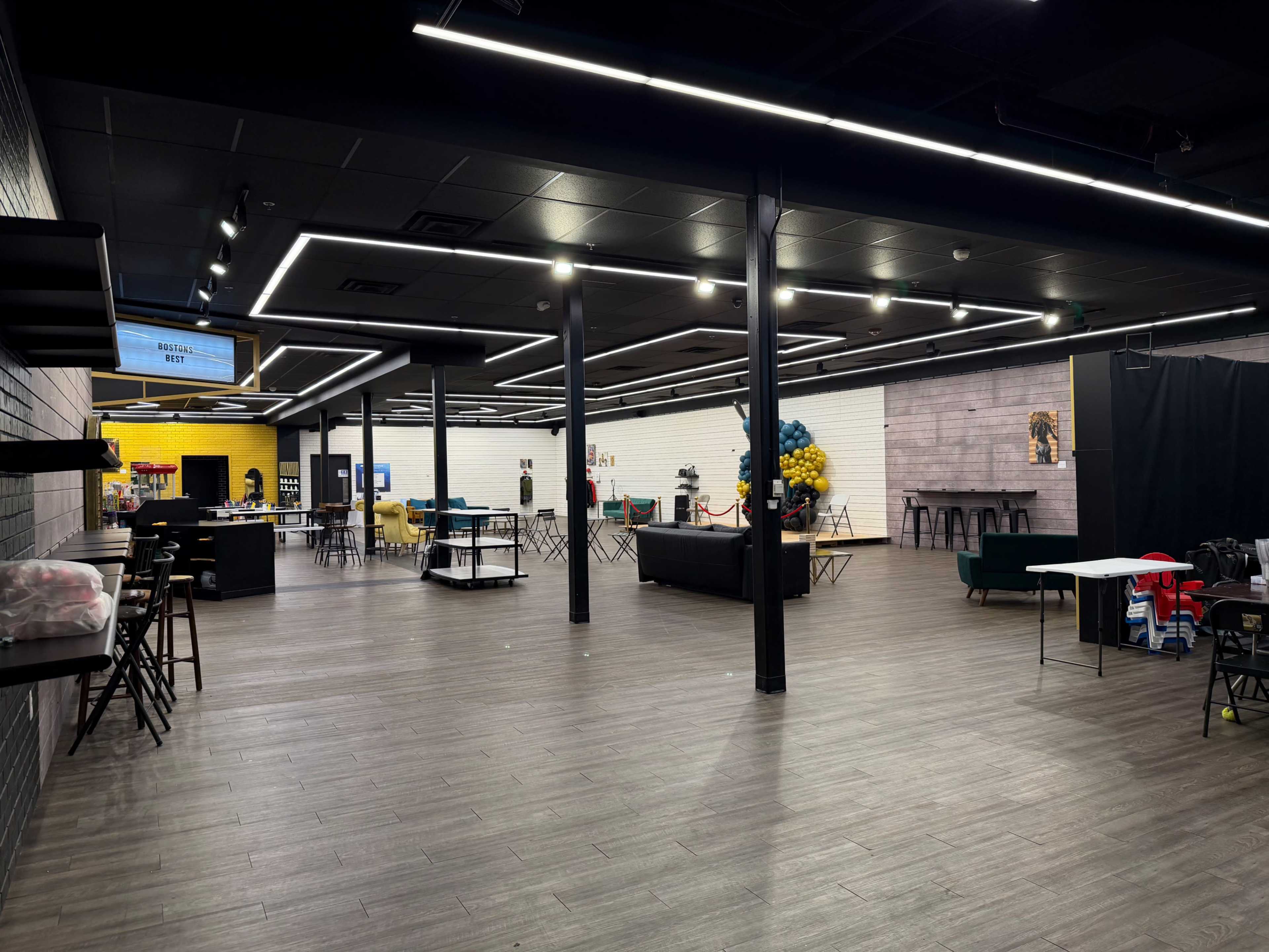 The image shows a spacious, modern indoor area with several tables, seating arrangements, and colorful decor elements.