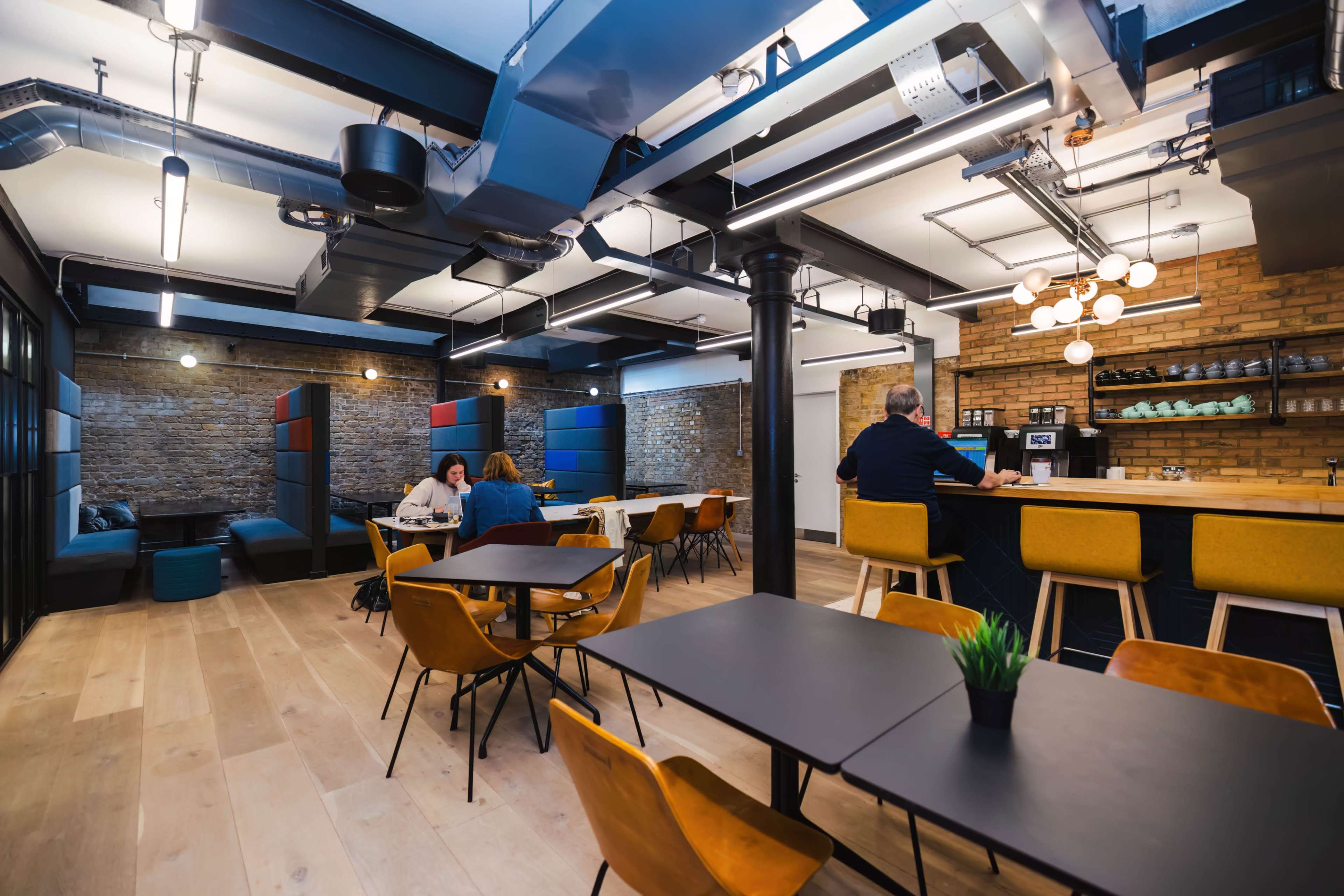 A modern office space with wood flooring, seating areas, and a coffee counter in a well-lit environment.