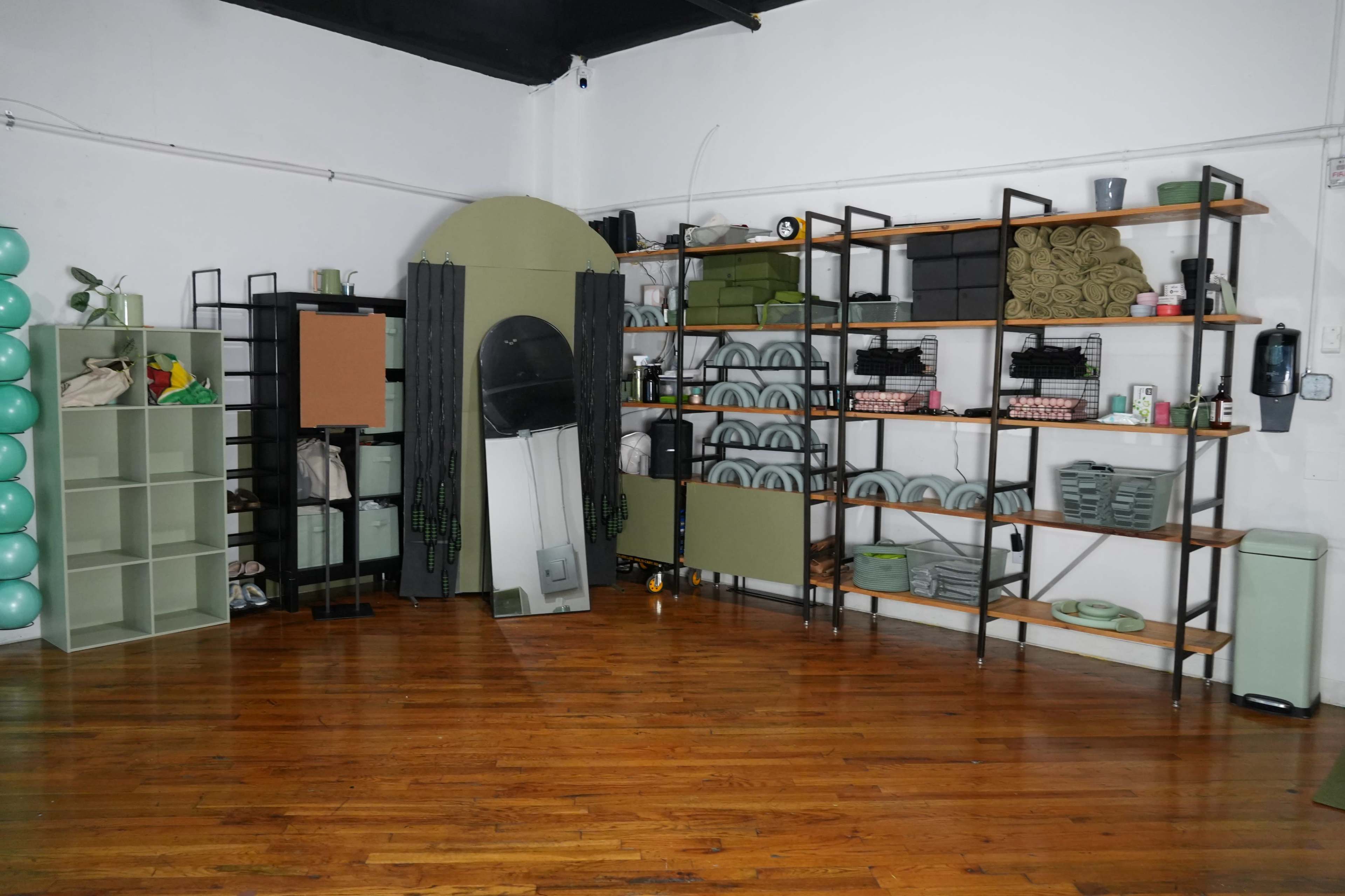 The image shows a spacious room featuring metal shelving units filled with various storage containers, towels, and equipment, set against a backdrop of wooden flooring.
