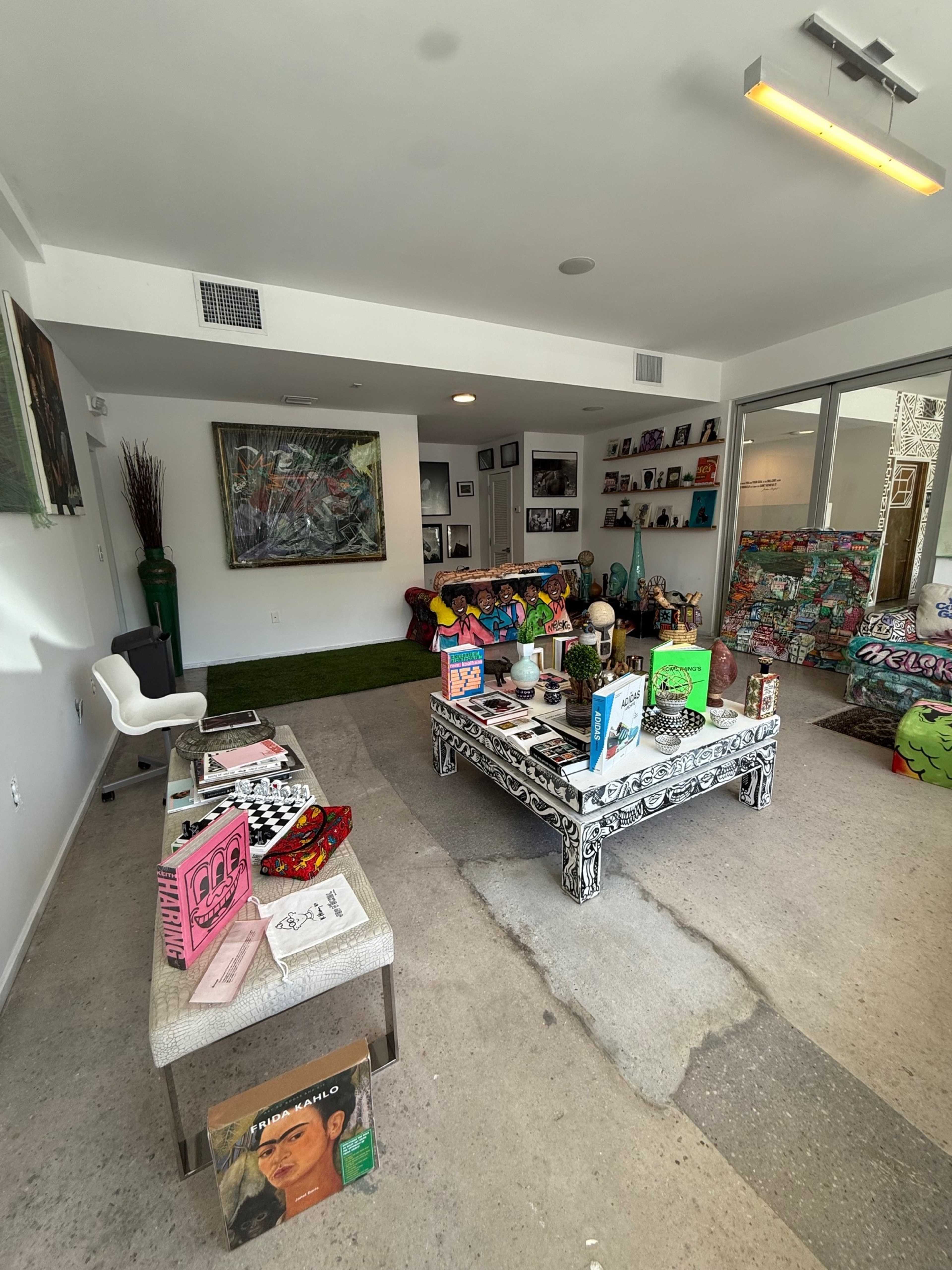 The image shows an eclectic living room with colorful furniture, art on the walls, and a coffee table displaying various books and decor items.