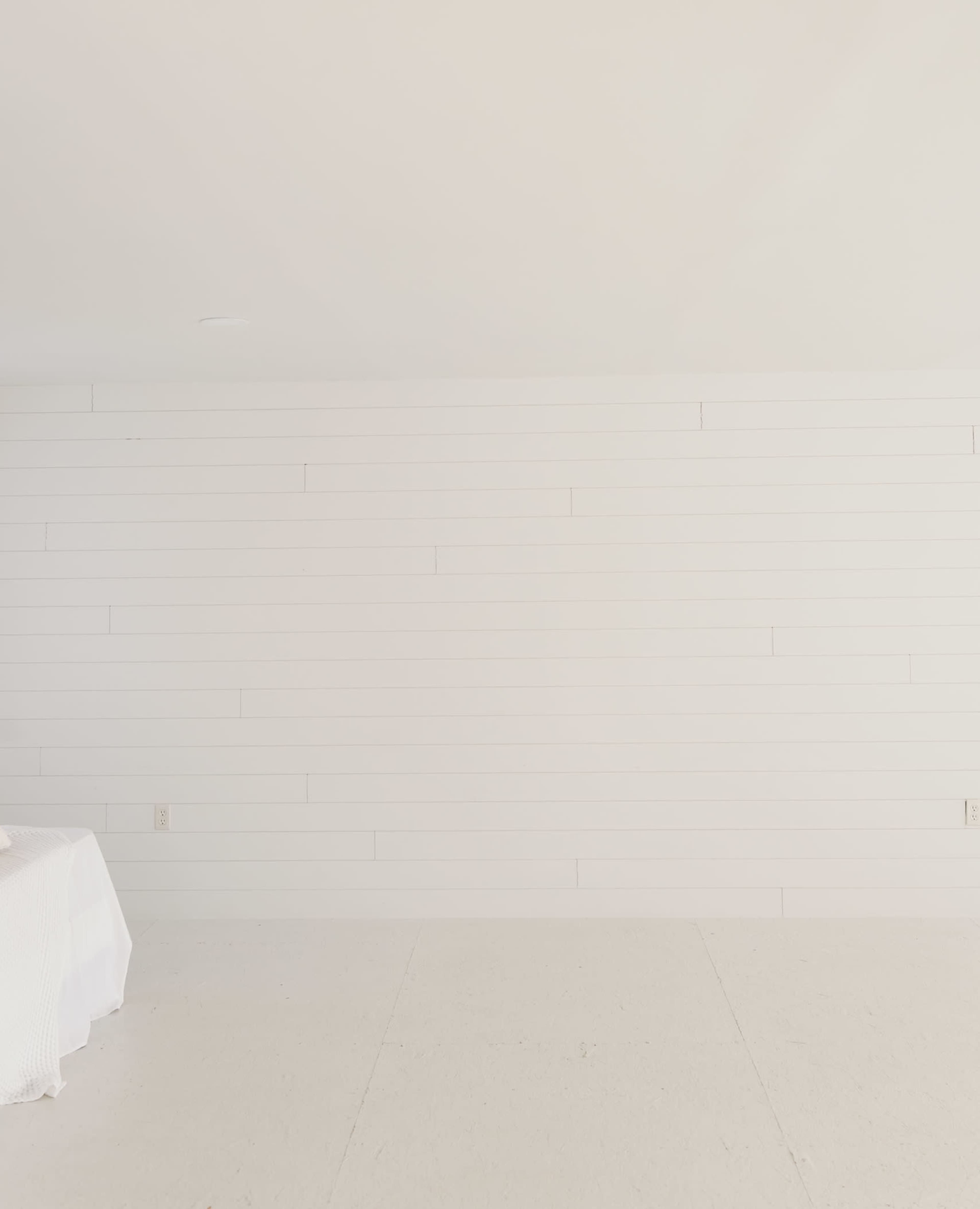 A spacious, minimalistic room features a white shiplap wall and a light-colored floor.