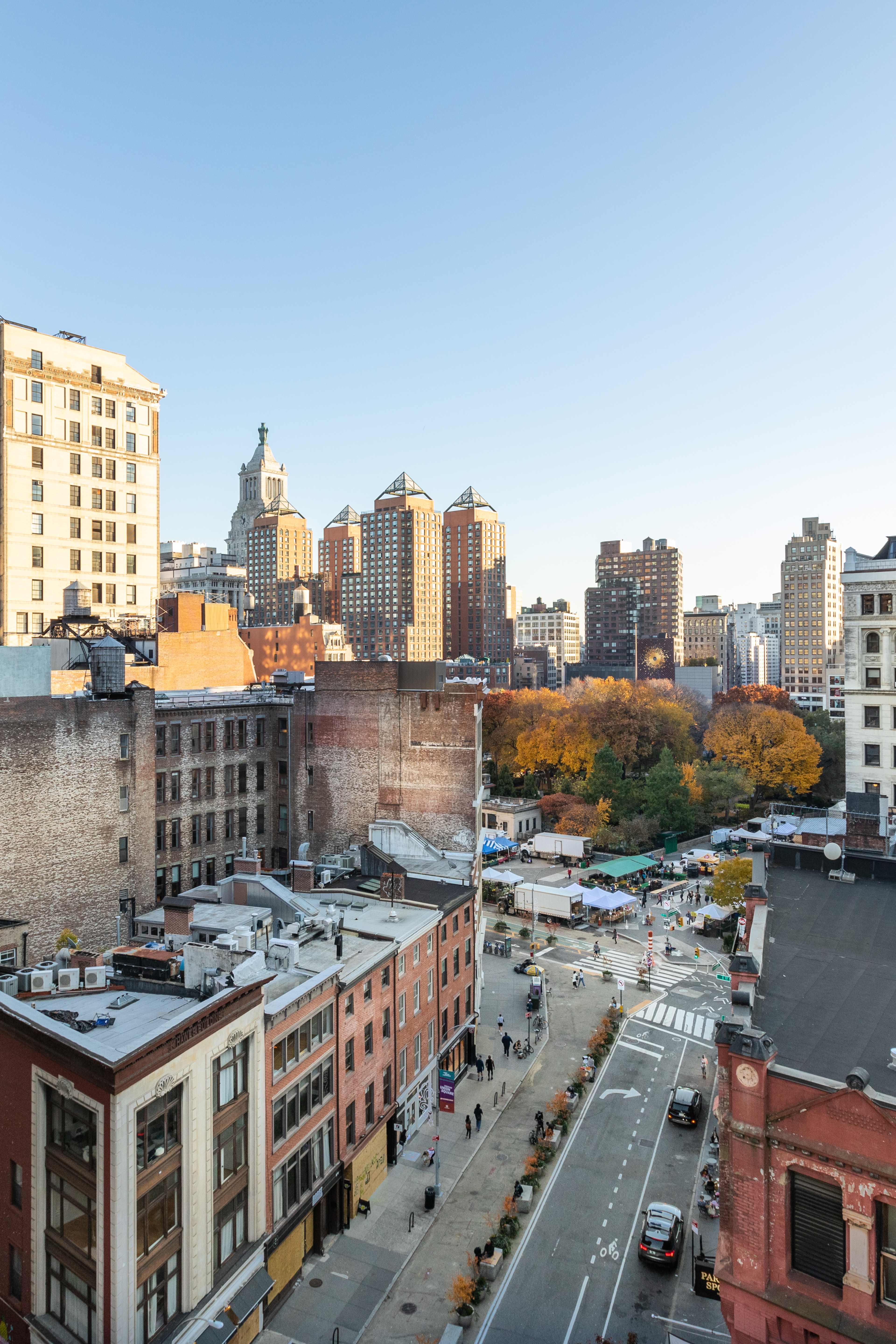 A high view of a cityscape with various buildings, a street lined with shops, and a park featuring autumn foliage.