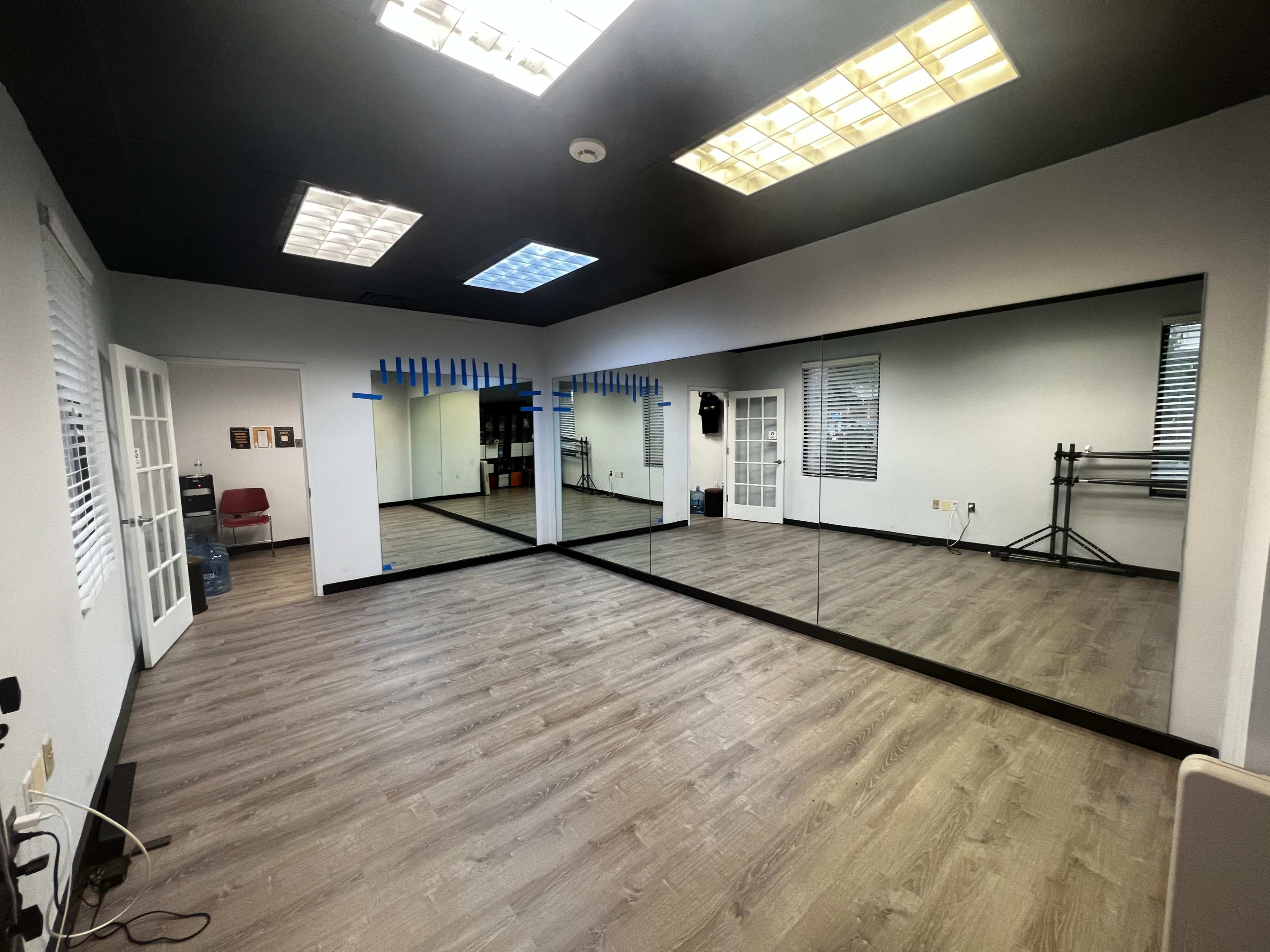 A spacious, well-lit studio with mirrored walls, wooden flooring, and large windows.