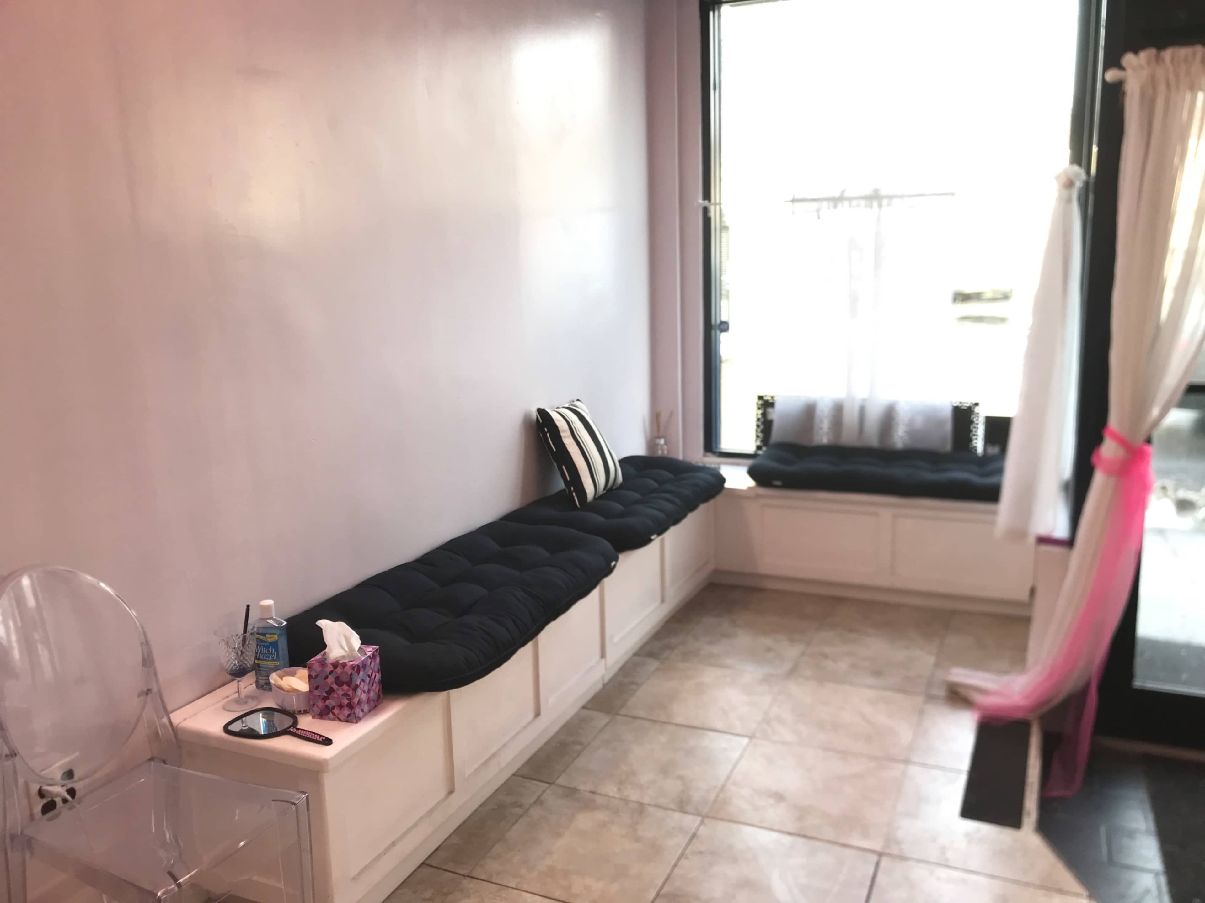 A bright room with a long, cushioned bench against the wall and a large window letting in natural light.