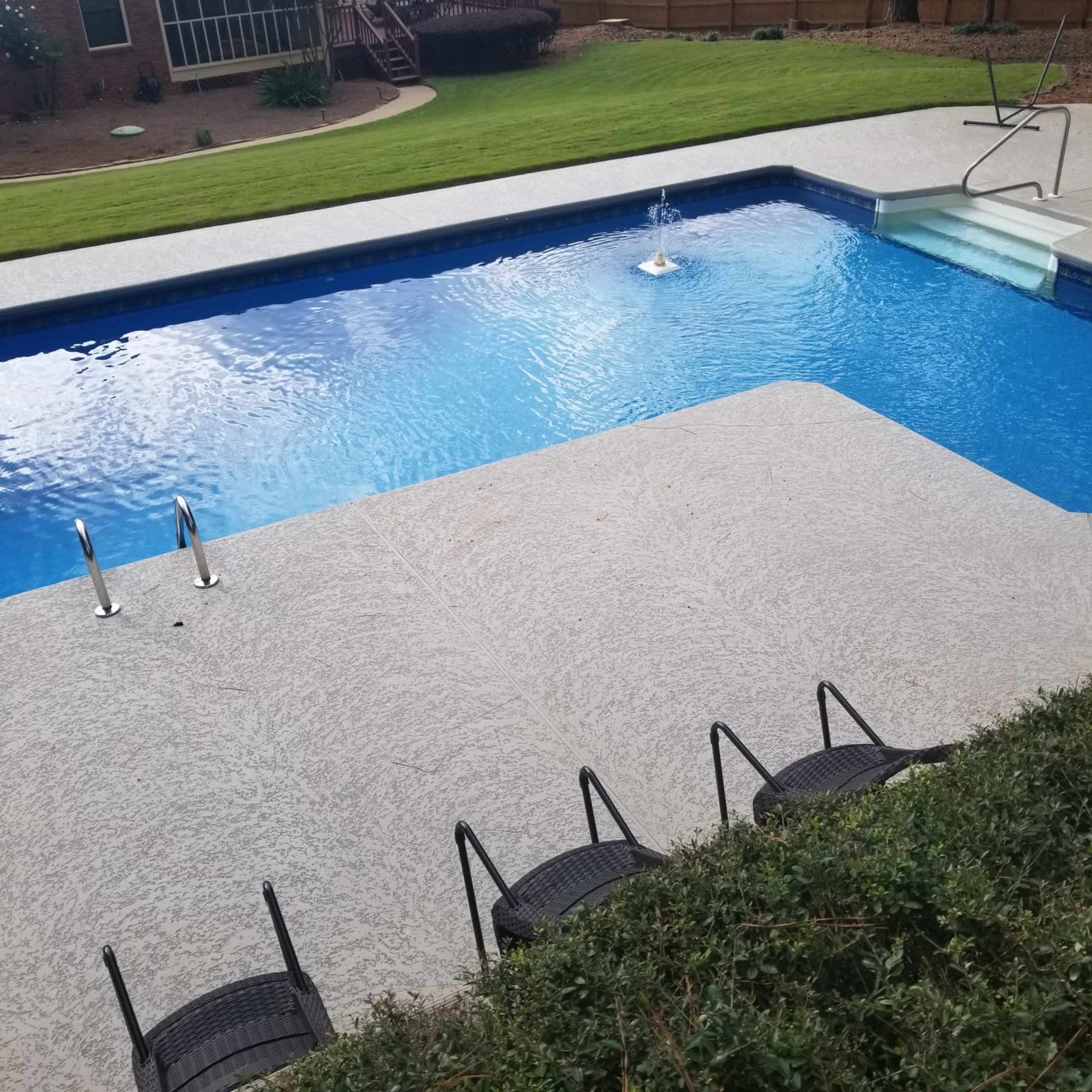 The image shows a swimming pool with a deck and several chairs arranged around it, surrounded by a grassy area.