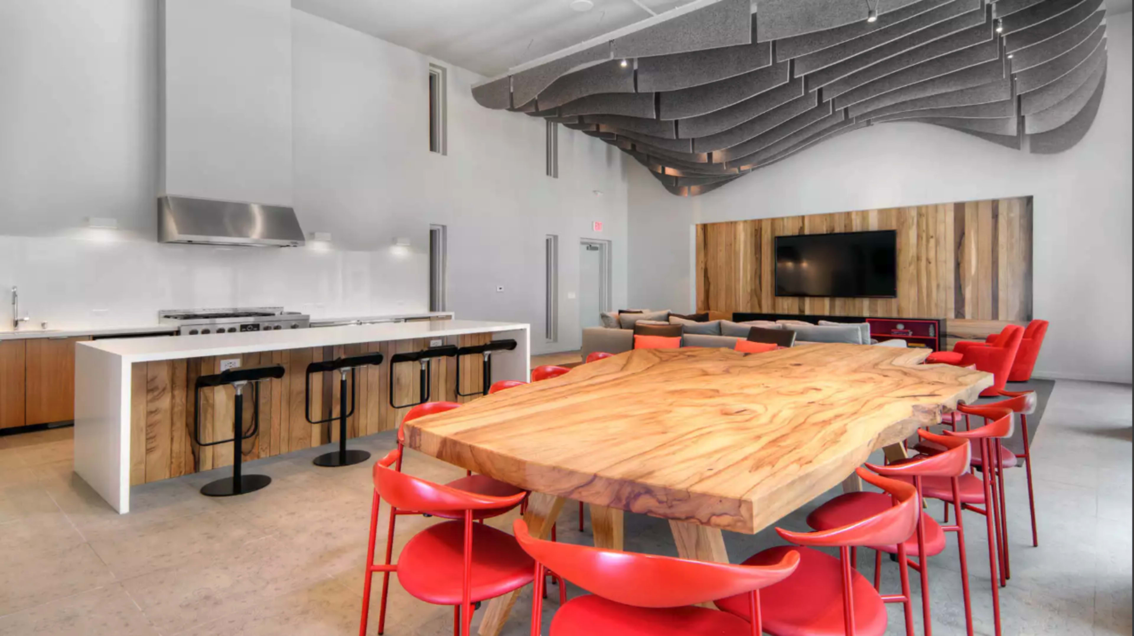 A modern kitchen and dining area featuring a large wooden table surrounded by red chairs, with a kitchen counter and sleek appliances in the background.