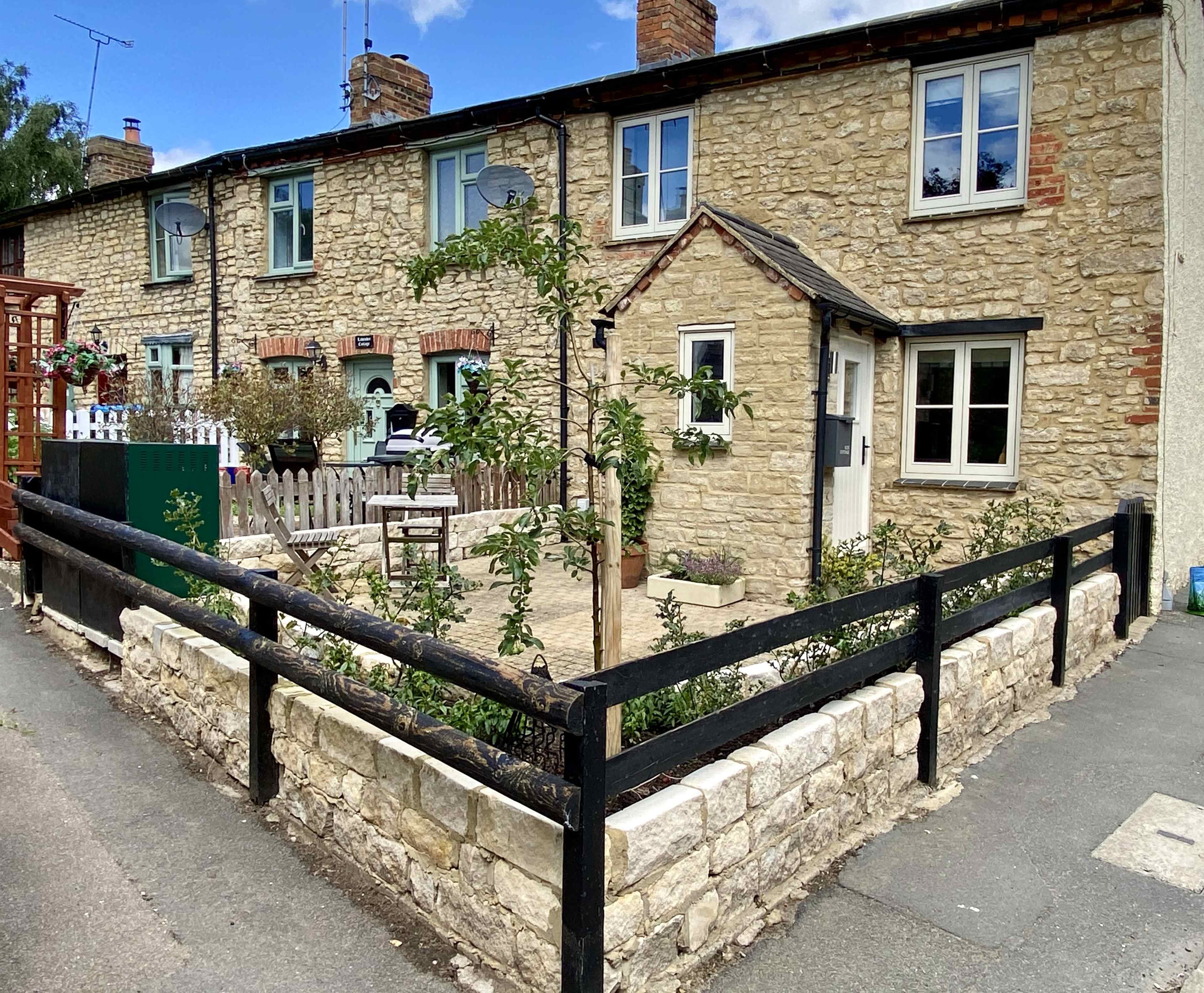 A stone cottage with a fenced garden and pathway along a quiet street.
