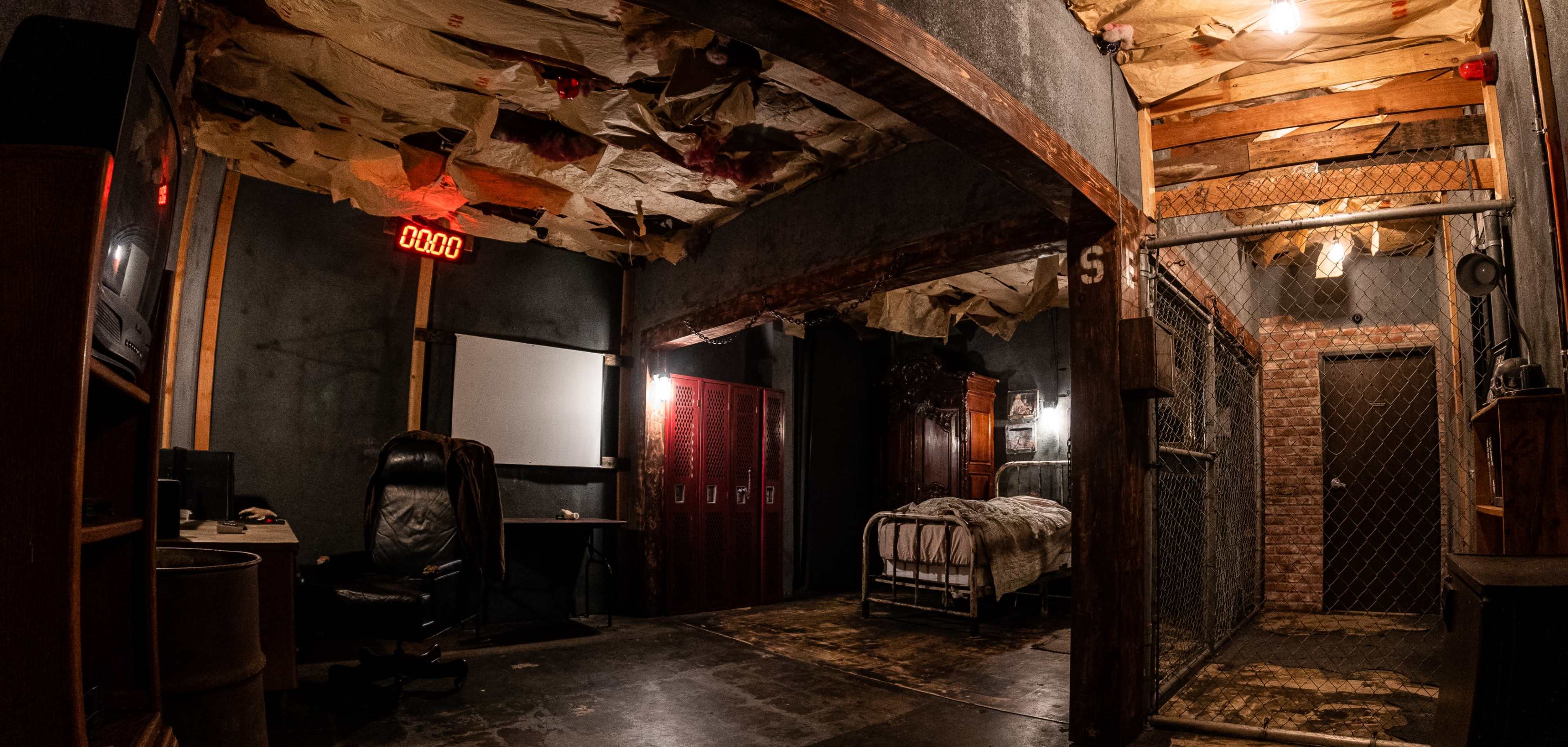 A dimly lit room with a wooden bed, a computer chair, lockers, and a clock displaying "00:00," all within a rustic interior featuring exposed beams and a ceiling covered with plastic sheets.