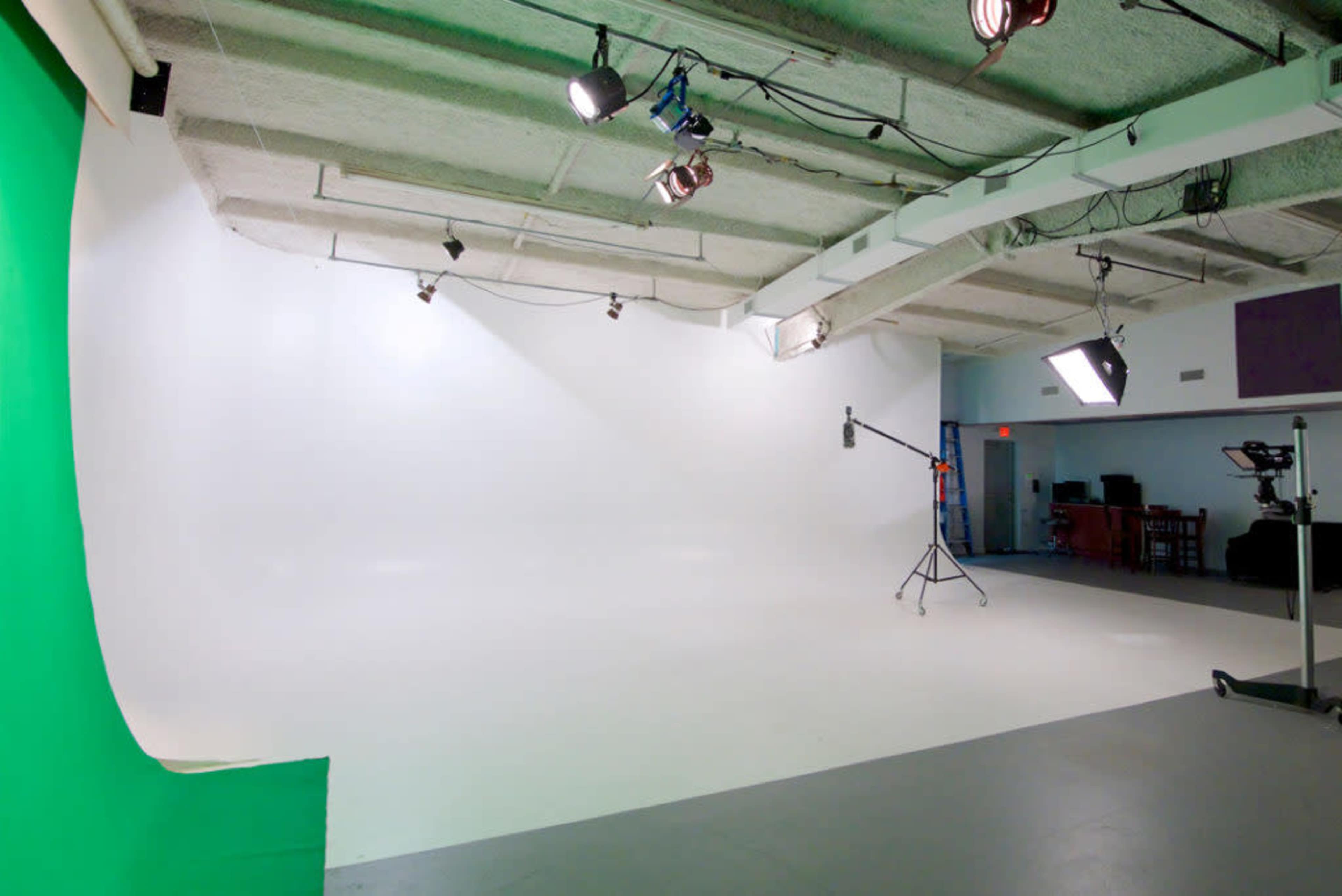 A photography studio with a green backdrop on one side and a white backdrop on the other, equipped with lighting and camera equipment.