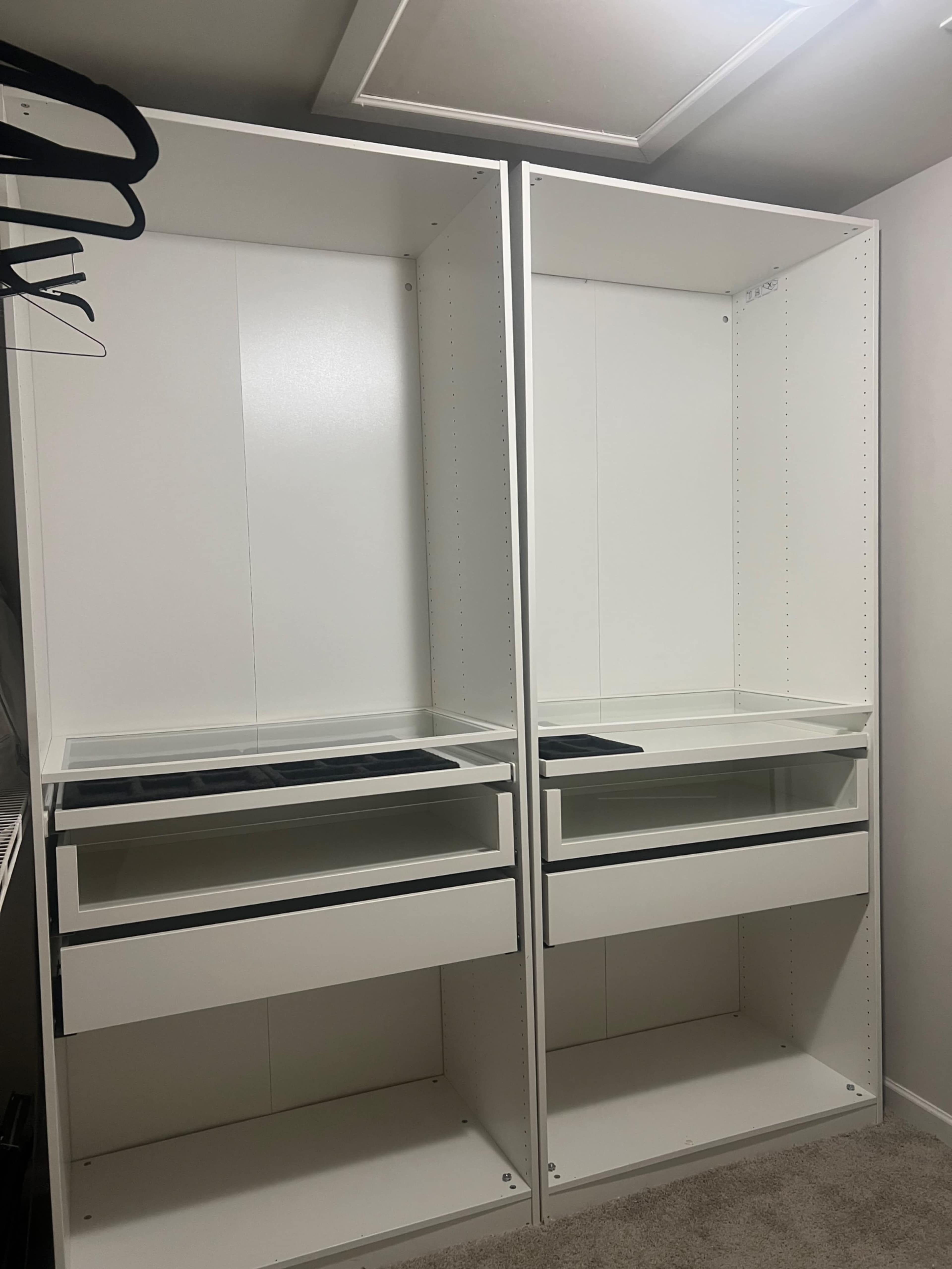 The image shows an empty closet with two tall white shelving units, each featuring open spaces and drawers at the bottom.