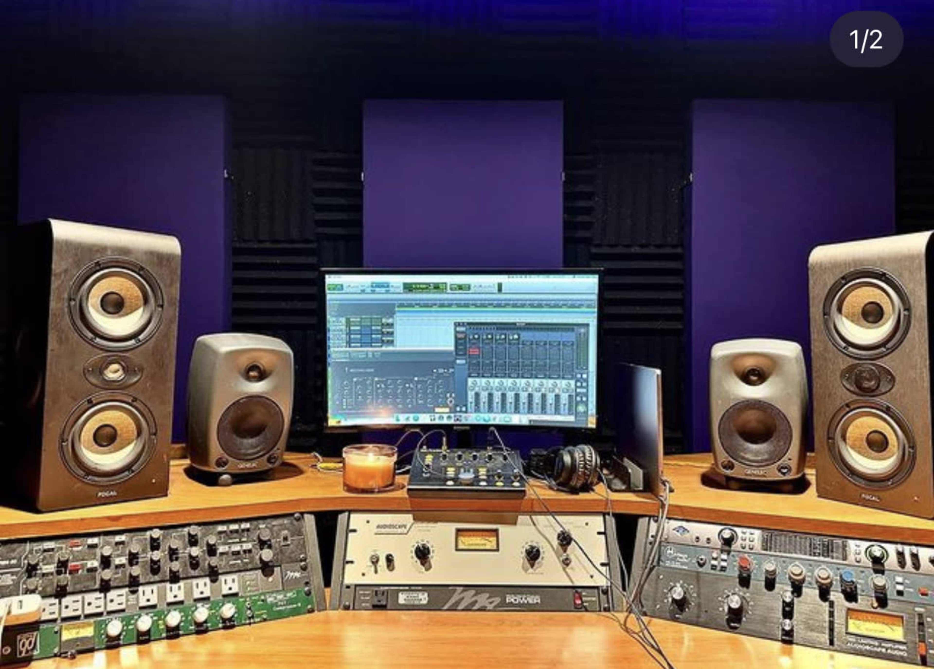 A home audio studio setup featuring speakers, a computer monitor displaying a digital audio workstation, and various audio equipment on a wooden desk.