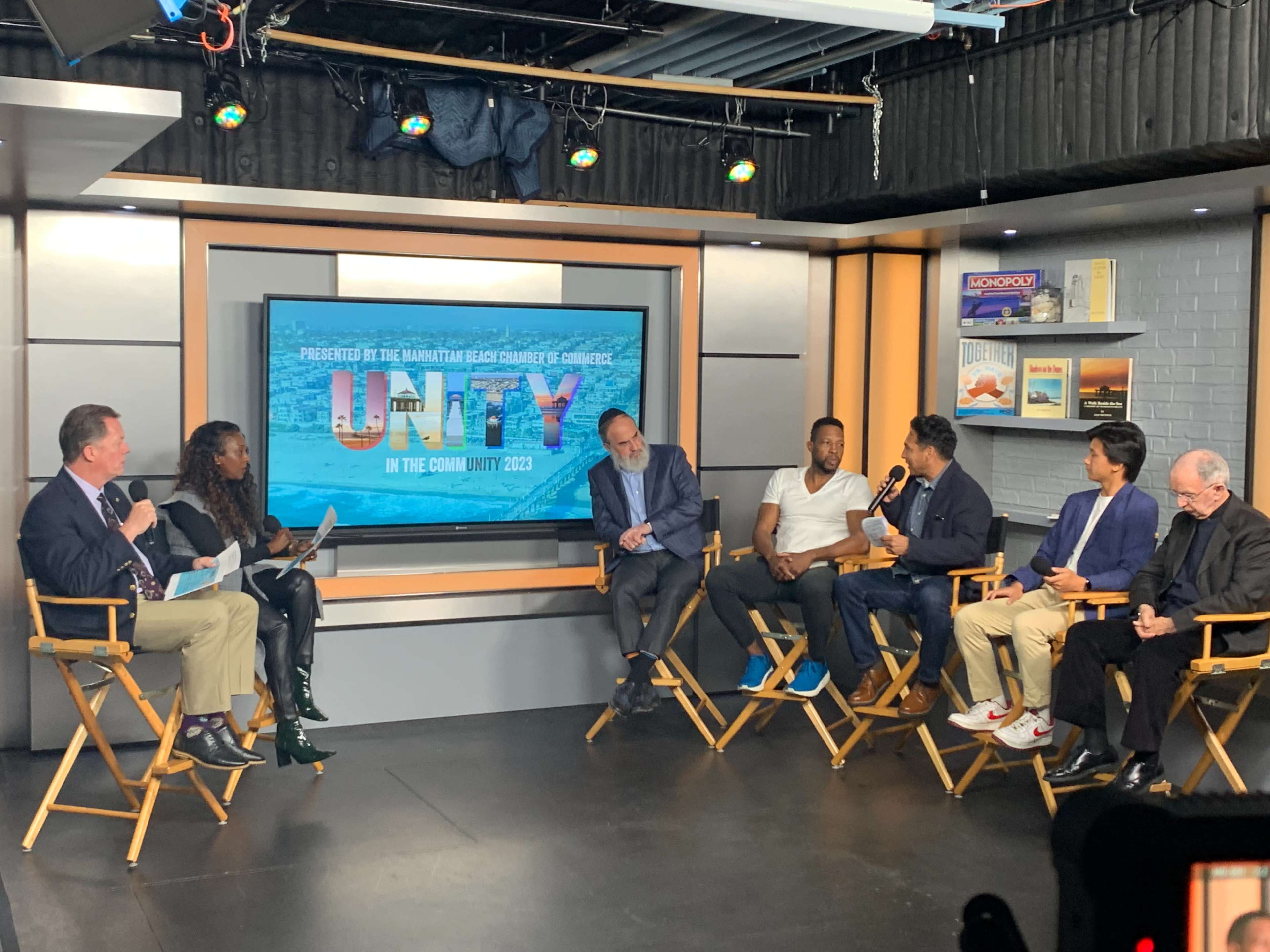 A panel discussion featuring several individuals seated in director's chairs in front of a screen displaying "Unity in the Community 2023."