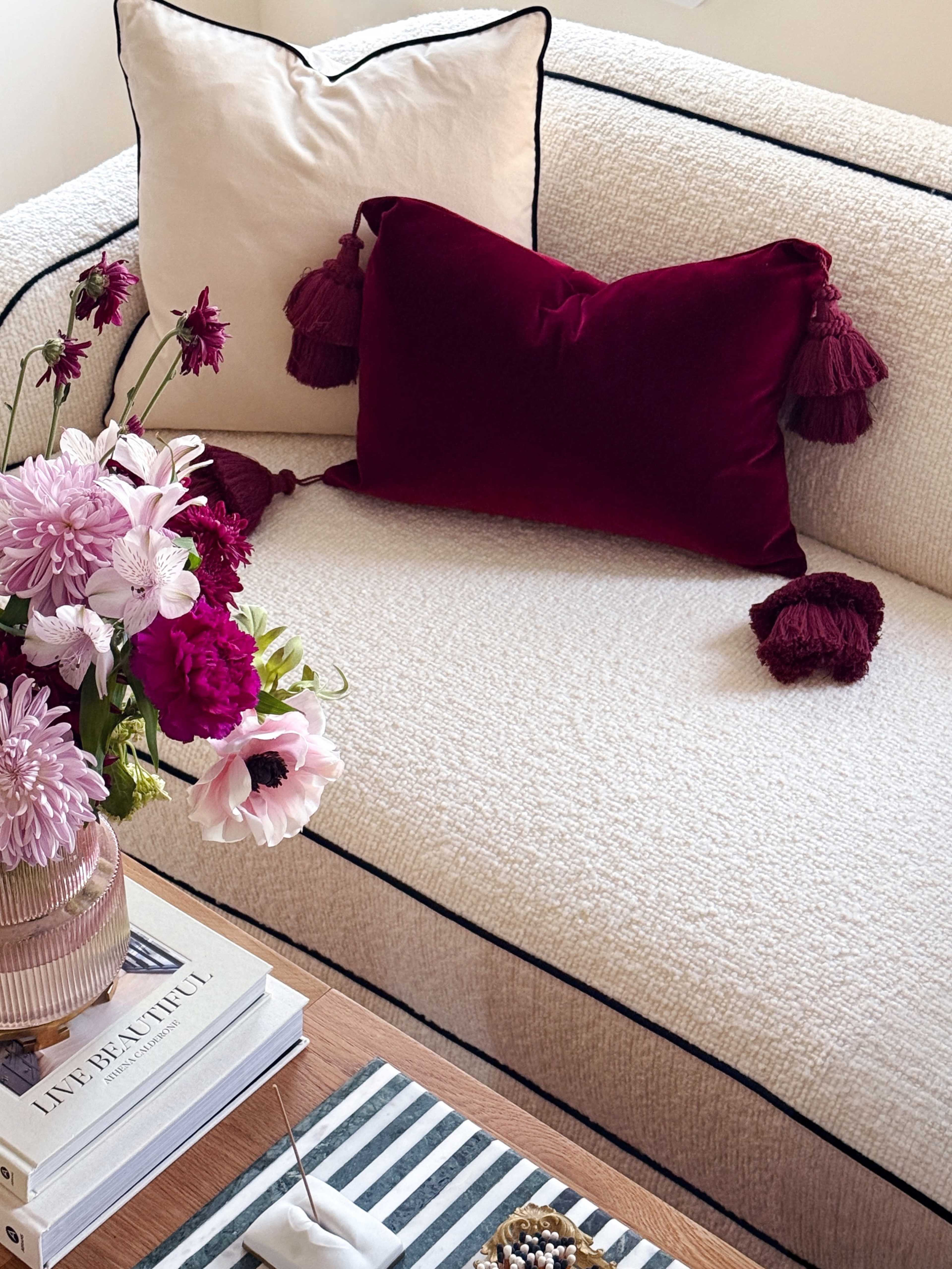 A beige sofa adorned with decorative pillows and a coffee table featuring books and flowers.