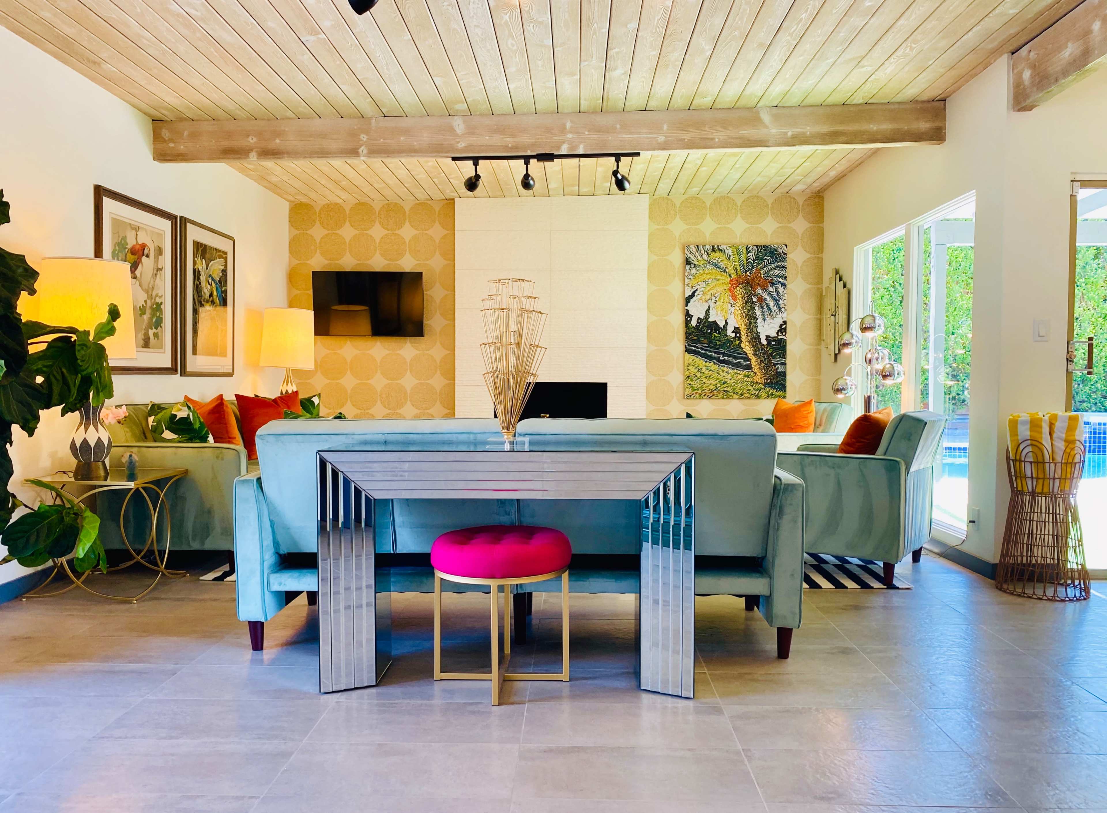 A modern living space features a light blue sofa, a glass table with a pink seat, and large windows that allow natural light to illuminate the room.