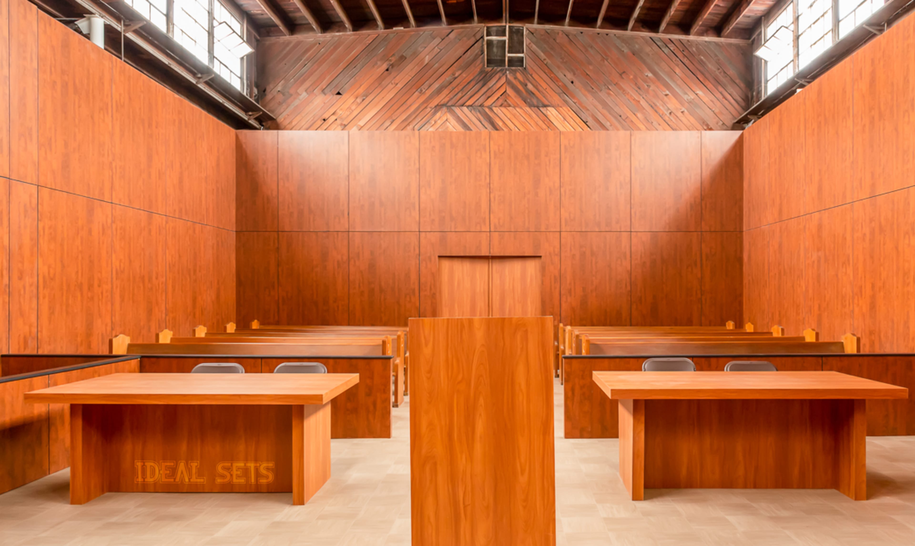 A wooden-paneled courtroom with several empty rows of benches and a central podium.