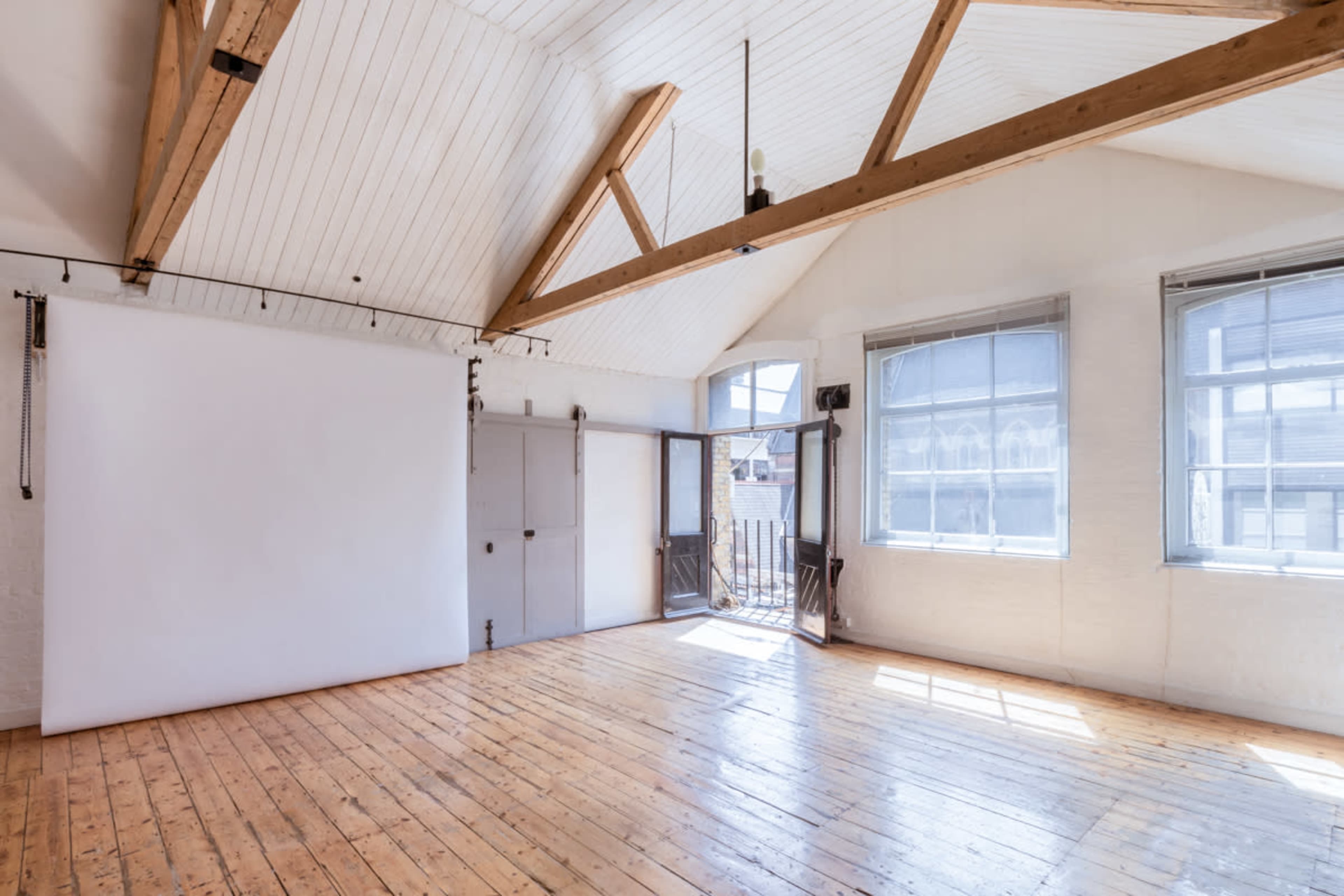 A spacious room with wooden flooring, large windows, and a blank wall suitable for photography.
