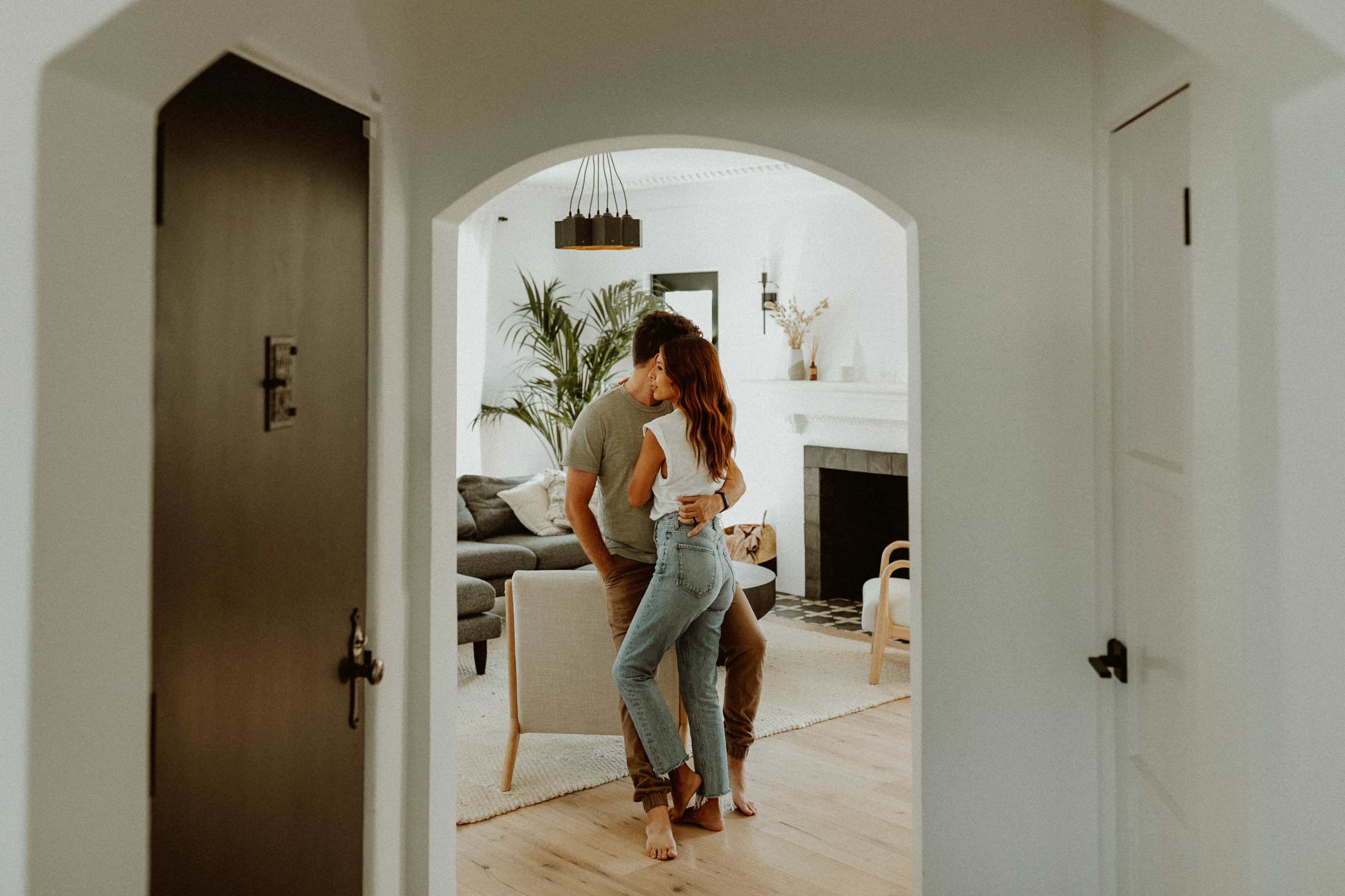 A couple shares a close embrace in a spacious living room framed by an arched doorway.