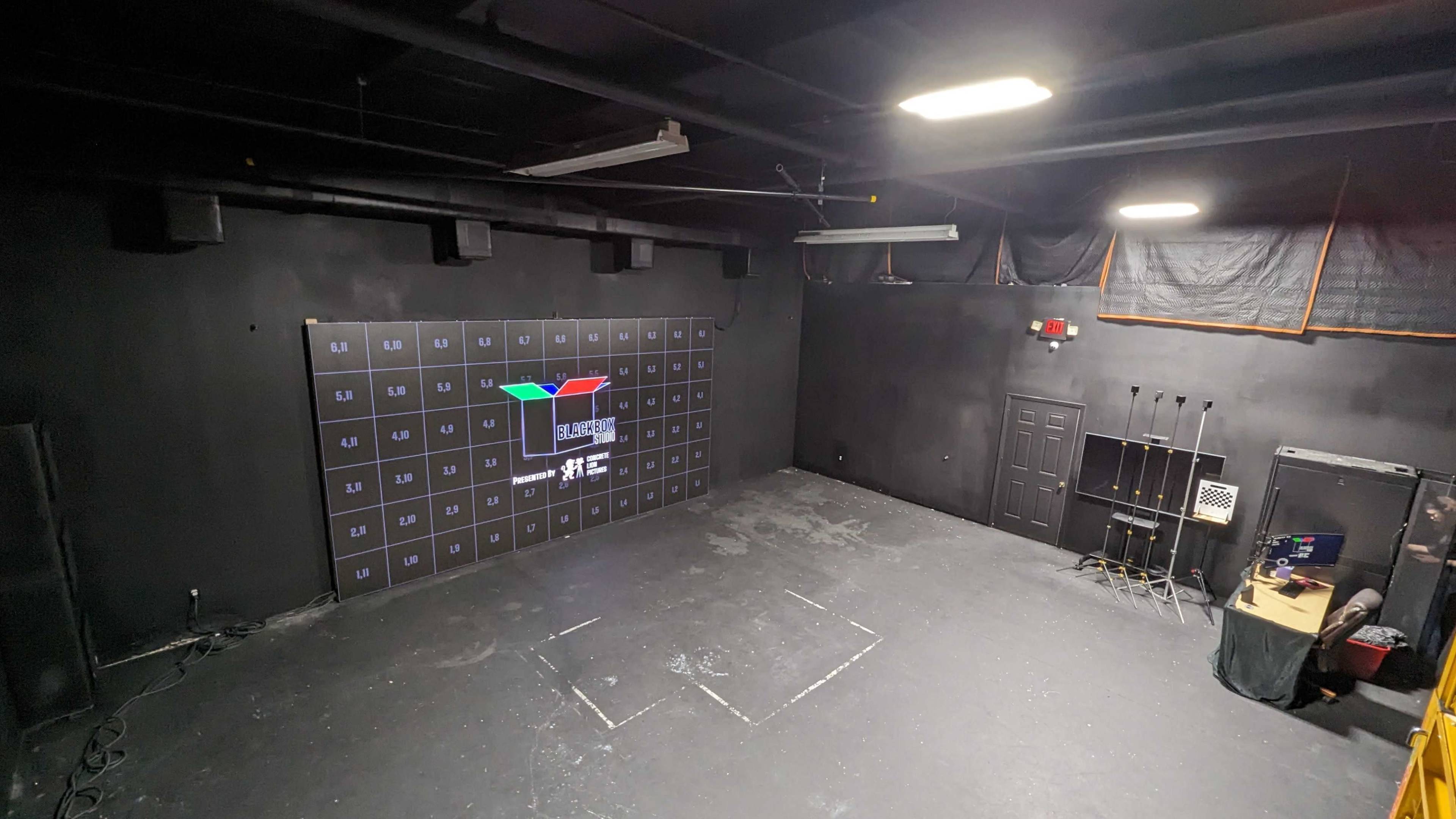 A large, empty black room with a grid of squares on one wall and a projection displaying "Scene" in the center.