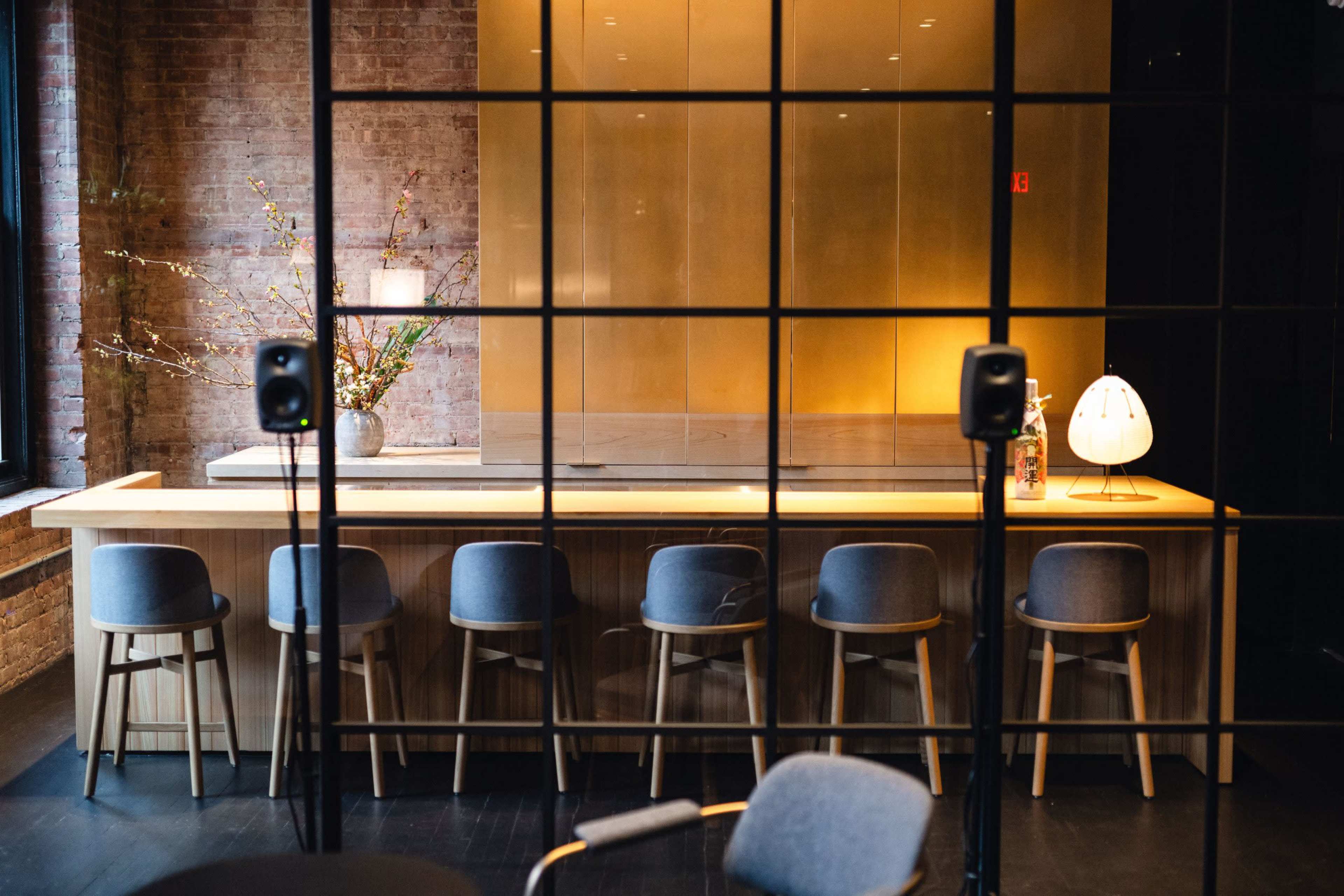 A modern bar area with wooden counter and stools is visible behind a grid-patterned glass partition, featuring a flower arrangement and soft lighting.