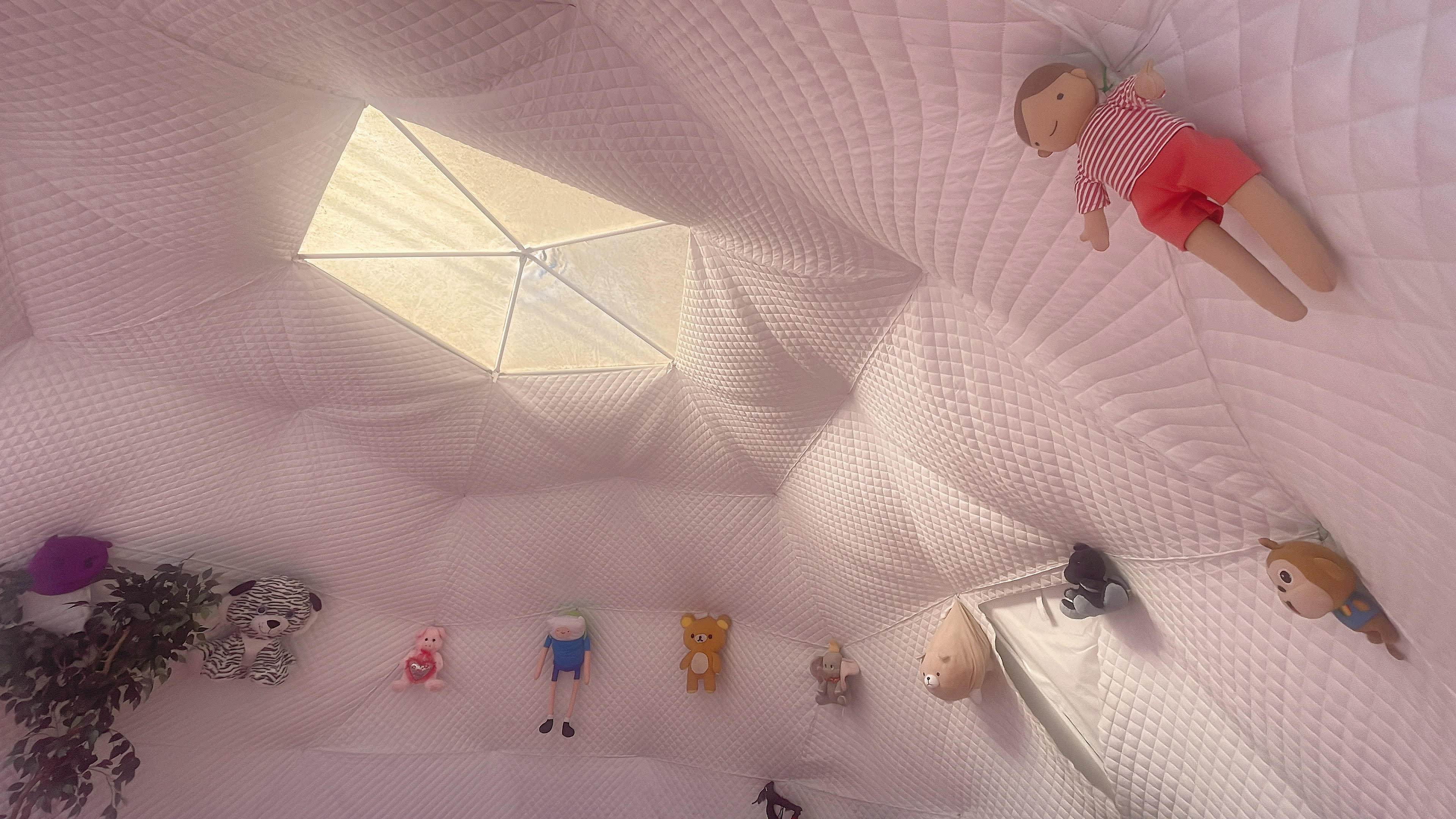The interior of a white tent features a skylight and various stuffed toys hanging from the walls.
