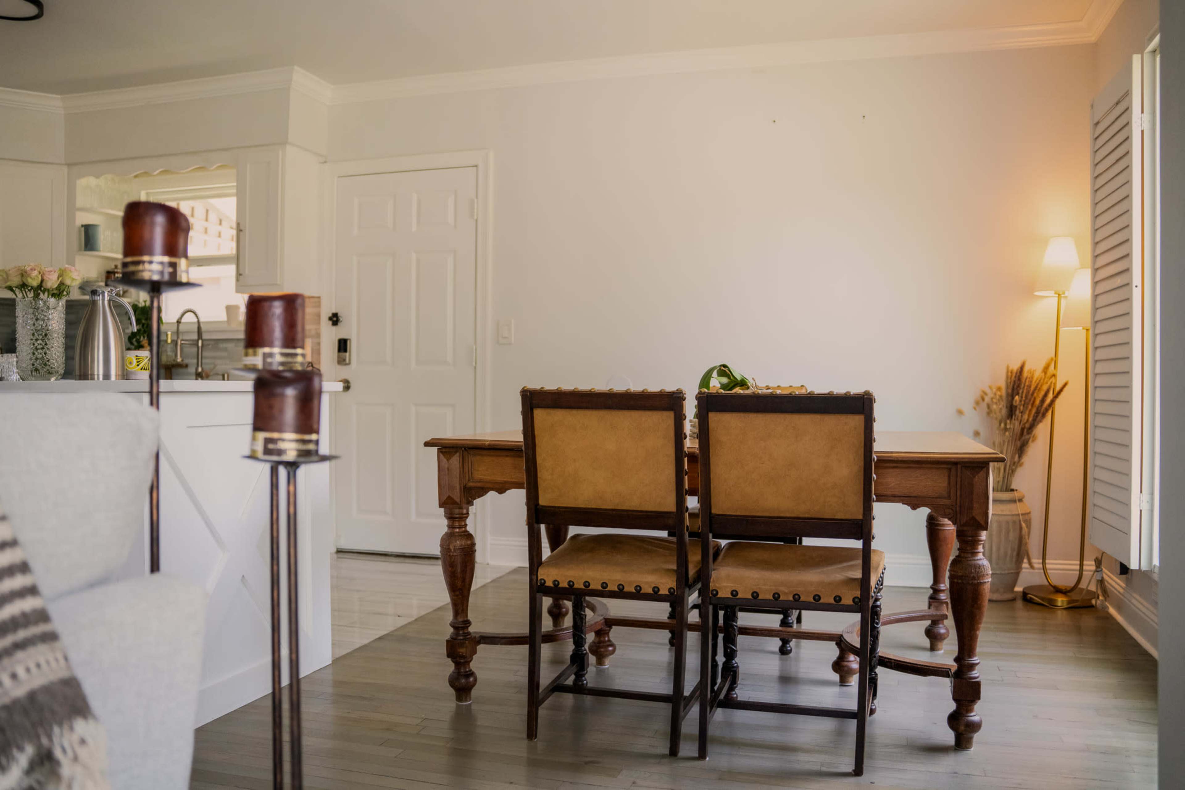 The image shows a dining area with a wooden table and two leather-upholstered chairs, set against a light-colored wall with a doorway visible.