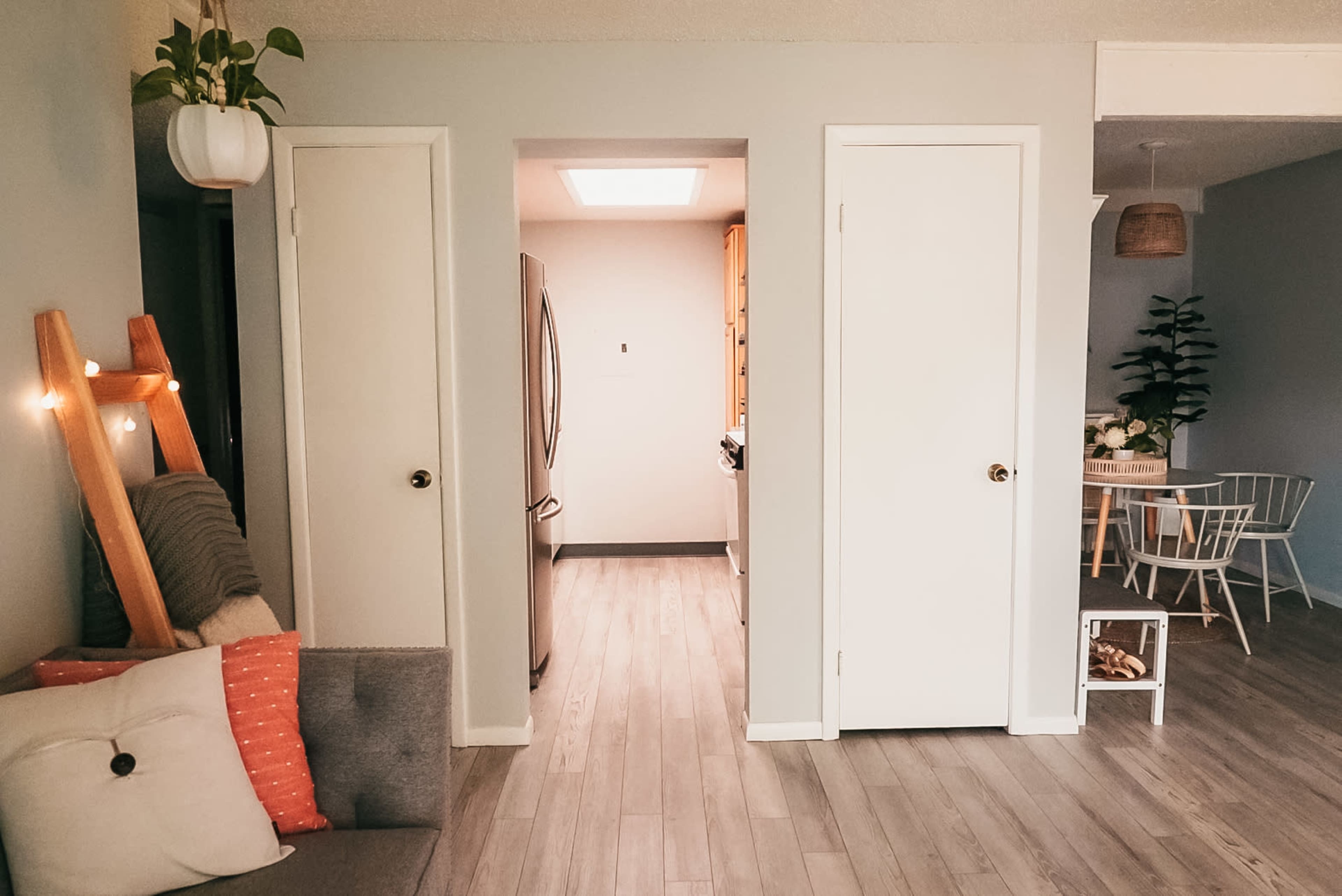 A cozy interior space with two closed doors, a small kitchen visible in the background, and a dining area with a table and chairs to the right.