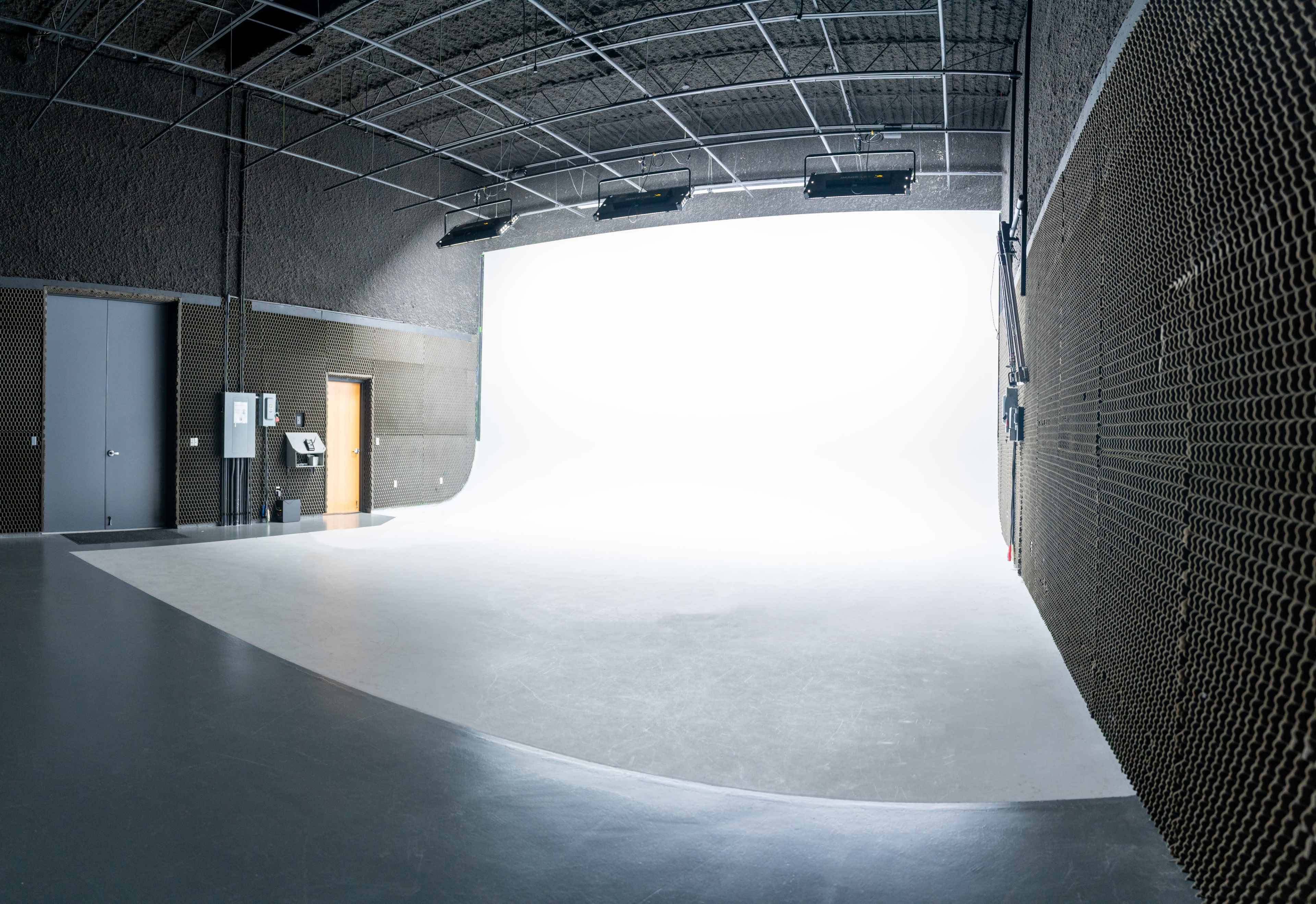 The image shows a spacious, empty studio with a seamless white backdrop and a high ceiling.