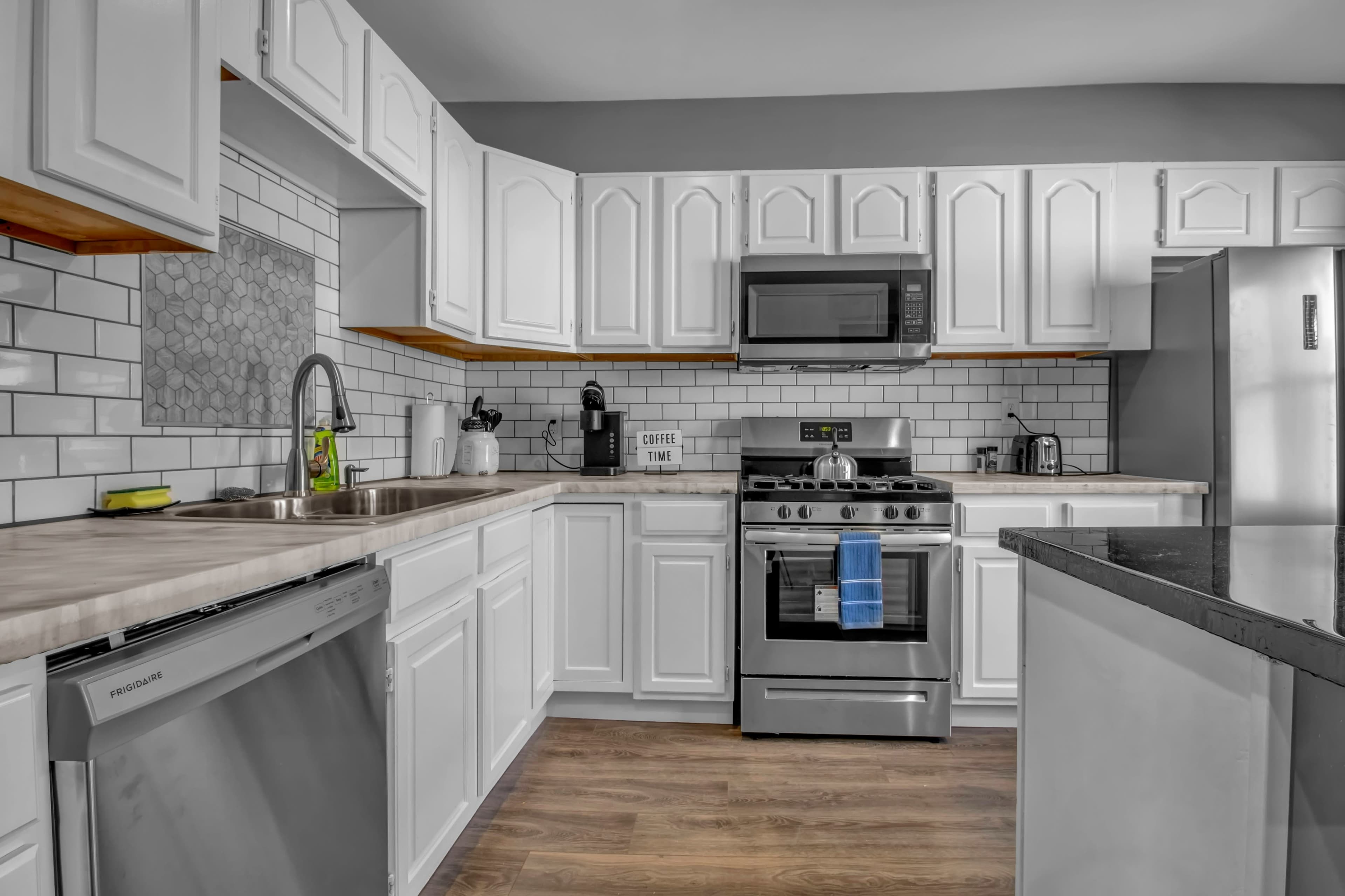A modern kitchen features white cabinetry, stainless steel appliances, and a beige countertop with a sink and dishwasher.