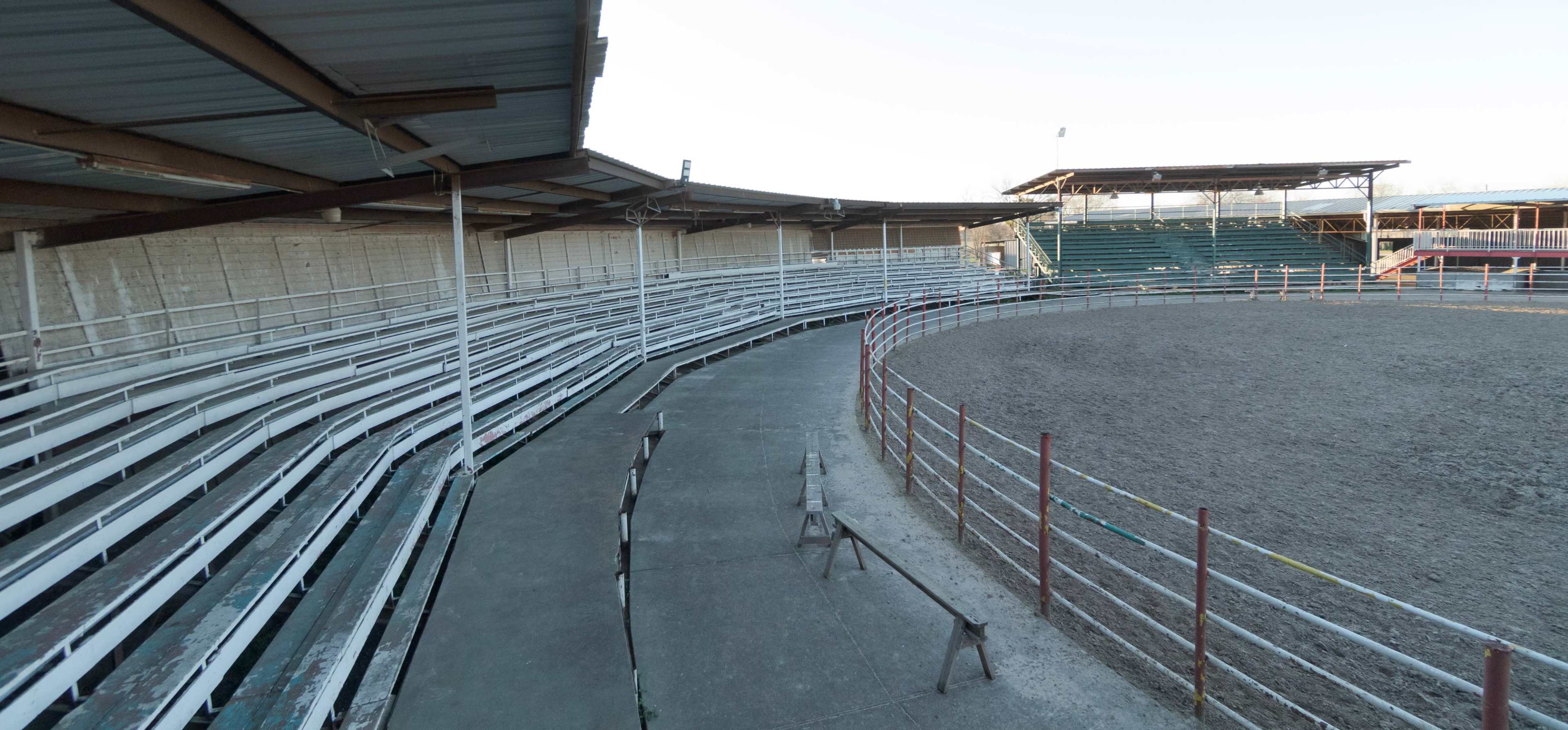 A partially empty rodeo arena with metal bleachers surrounding a circular dirt floor.