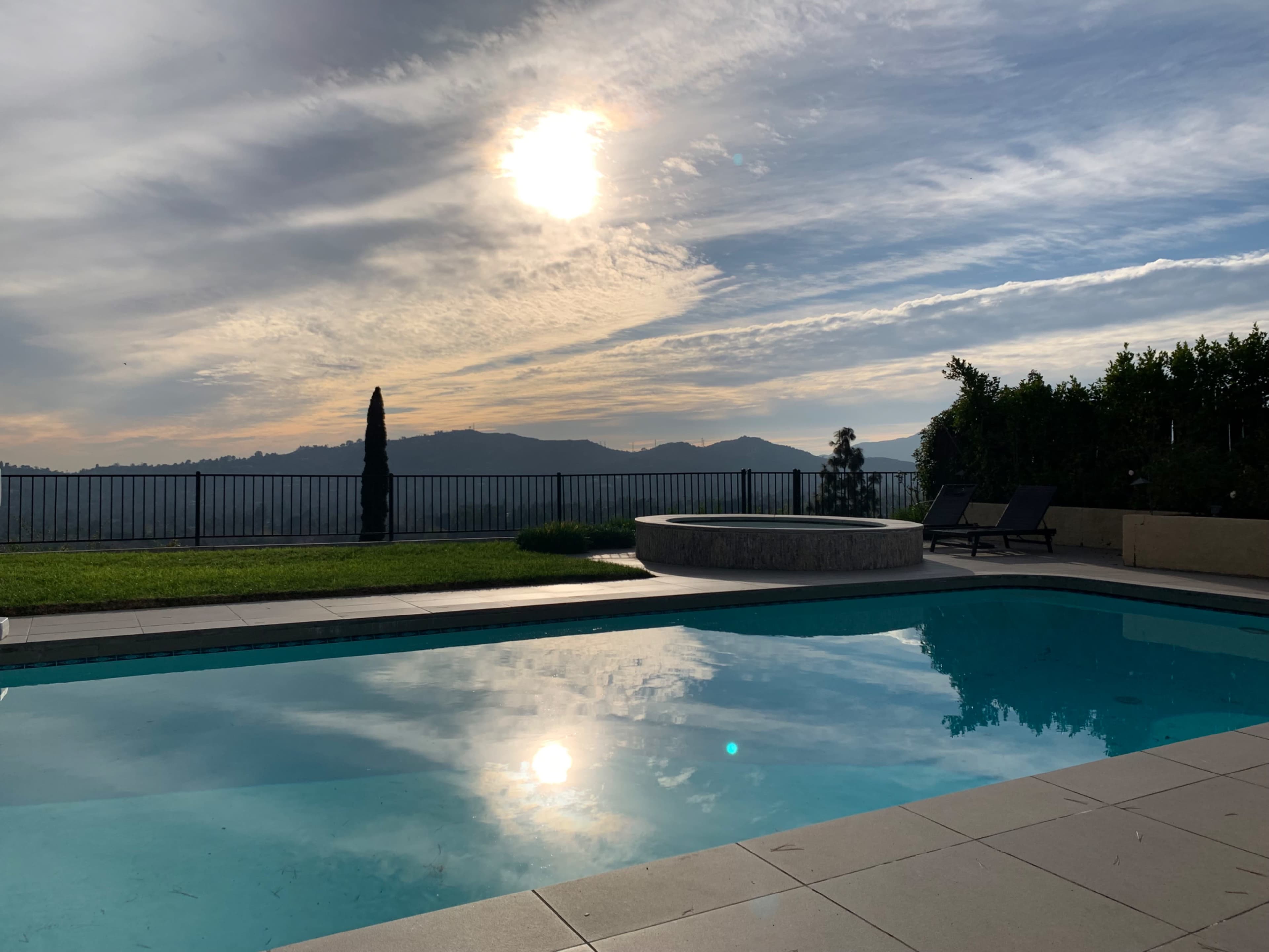 A serene pool reflecting the sun and surrounding hills under a partly cloudy sky.