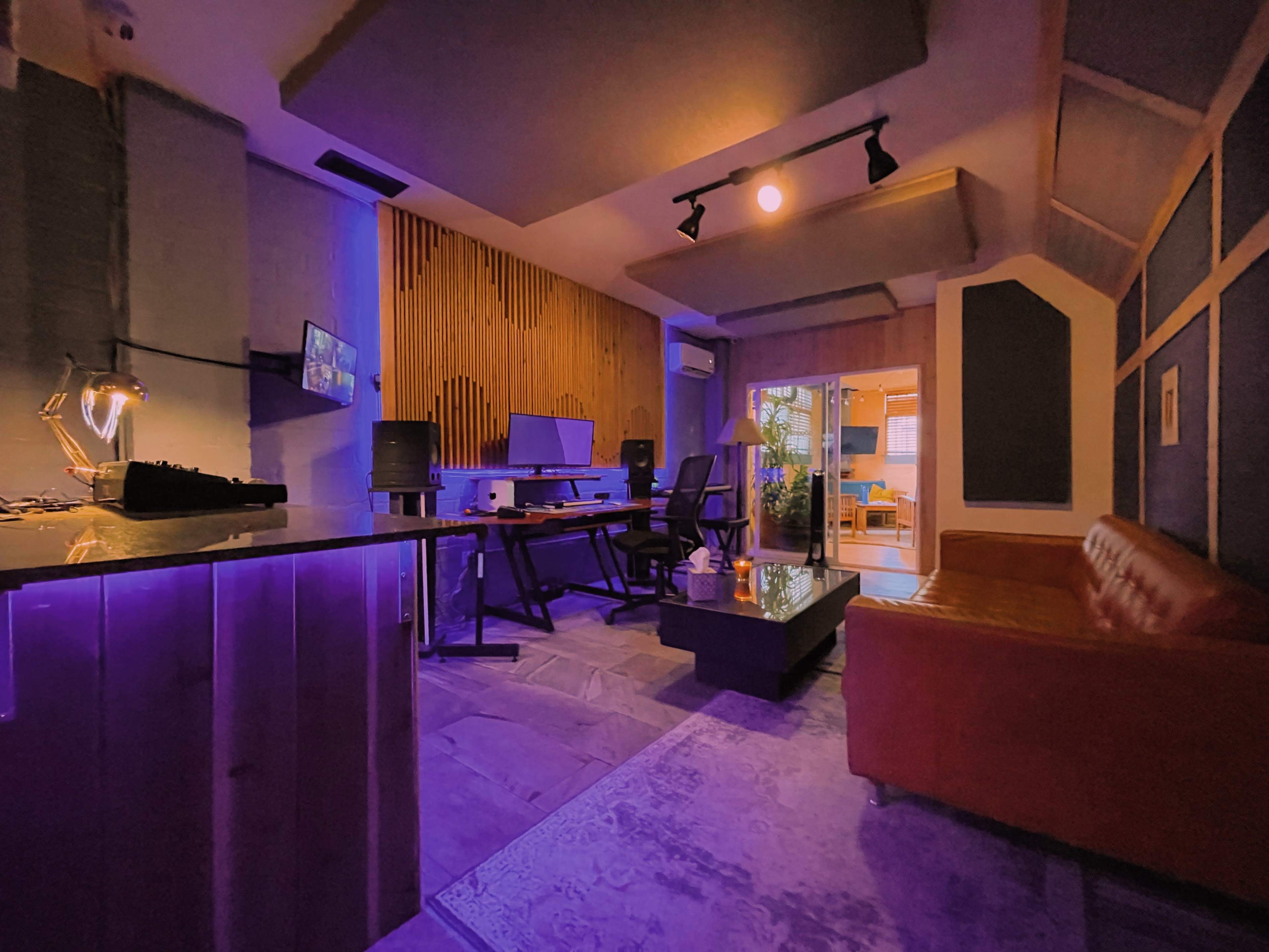 A modern recording studio featuring a red couch, multiple audio monitors, and a glass table under soft lighting.