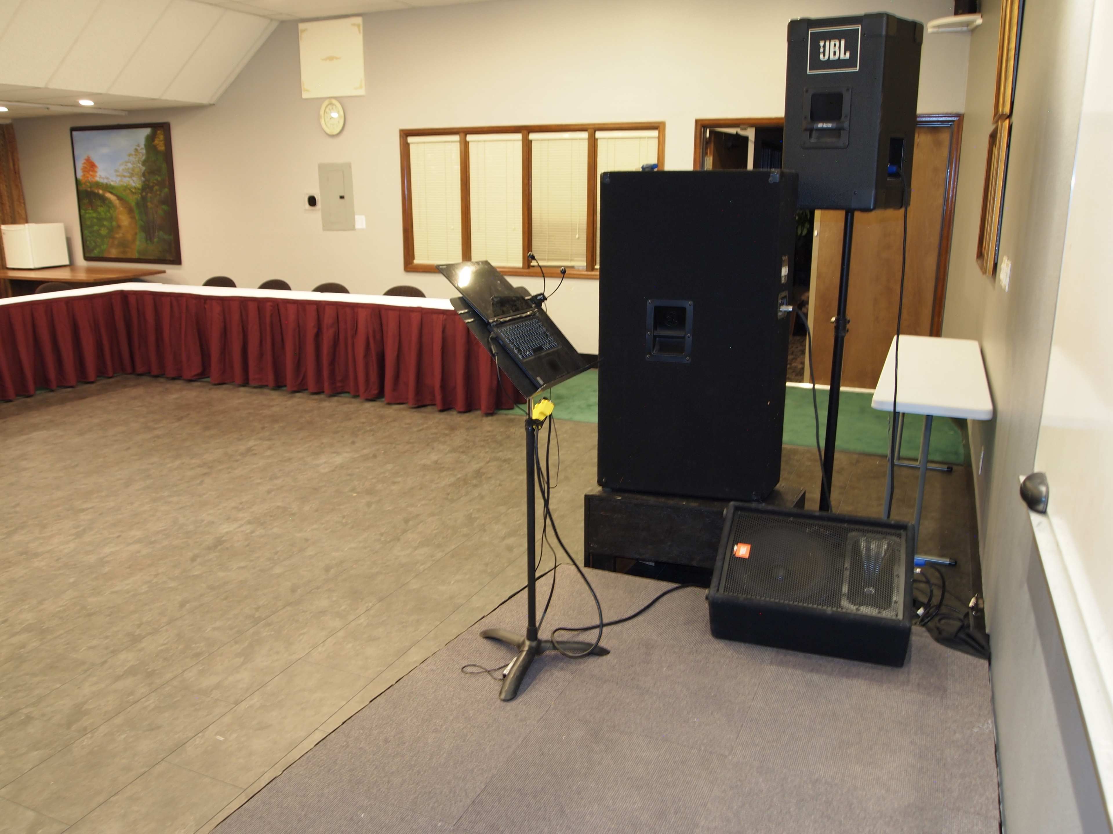 A small conference room with a sound system setup, featuring speakers, a microphone stand, and a long table covered with a maroon tablecloth.