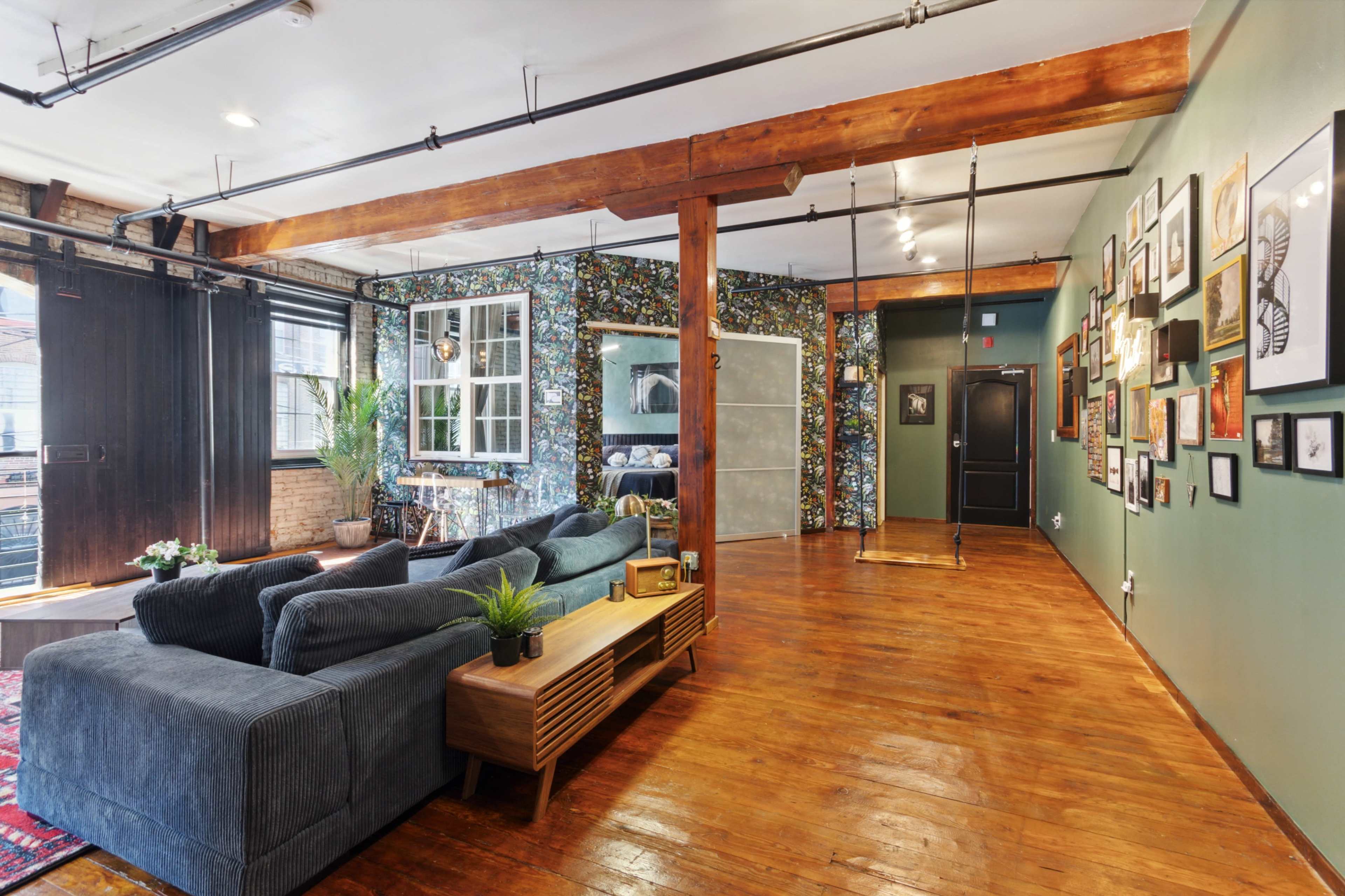 A spacious interior living area featuring a gray sectional sofa, a wooden coffee table, and a gallery wall of framed art beside a swing hanging from the ceiling.