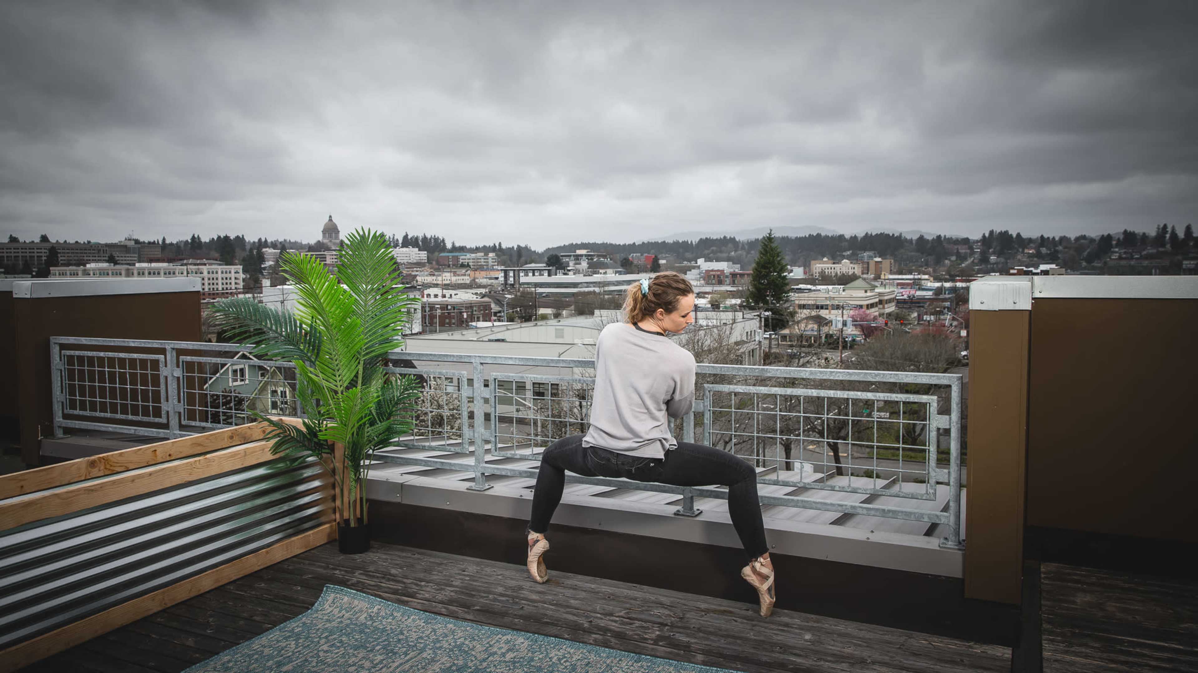 A dancer performs an acrobatic pose on the edge of a rooftop with a cityscape in the background.