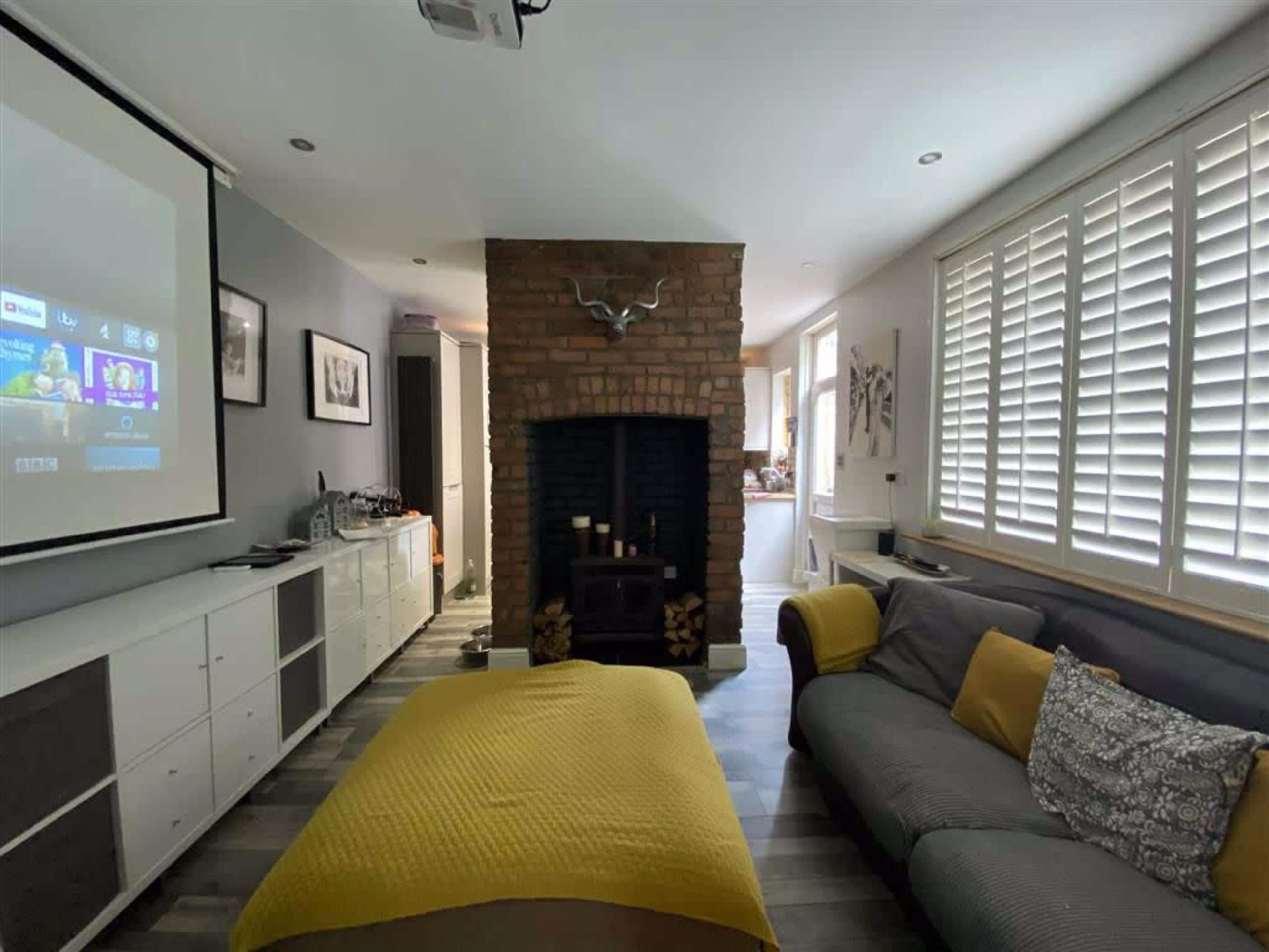 A modern living room with a large projector screen, a brick fireplace, and a gray sofa adorned with decorative pillows and a yellow throw.