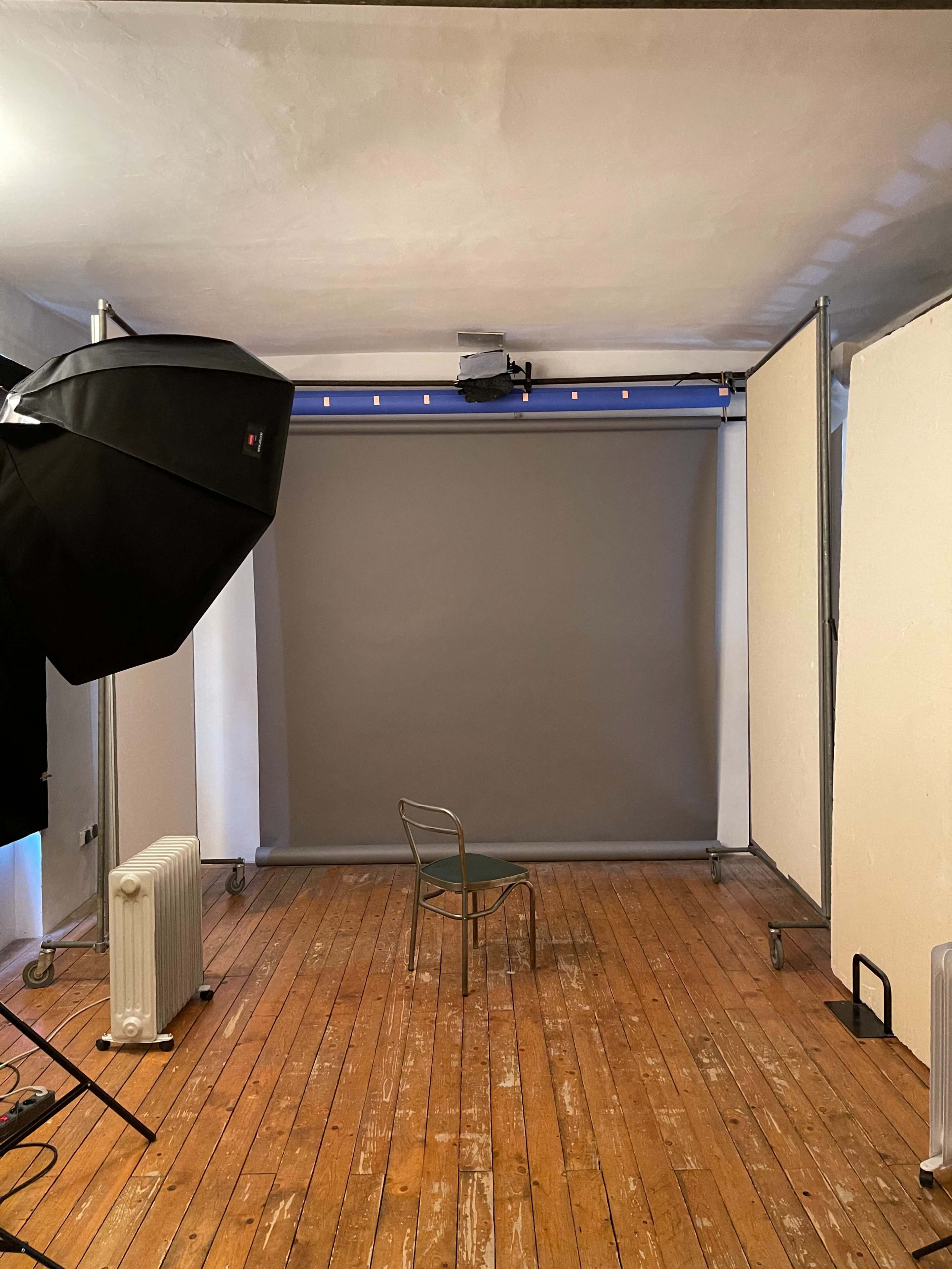 A photography studio with a gray backdrop, a chair in the center, and studio lights positioned around the space.