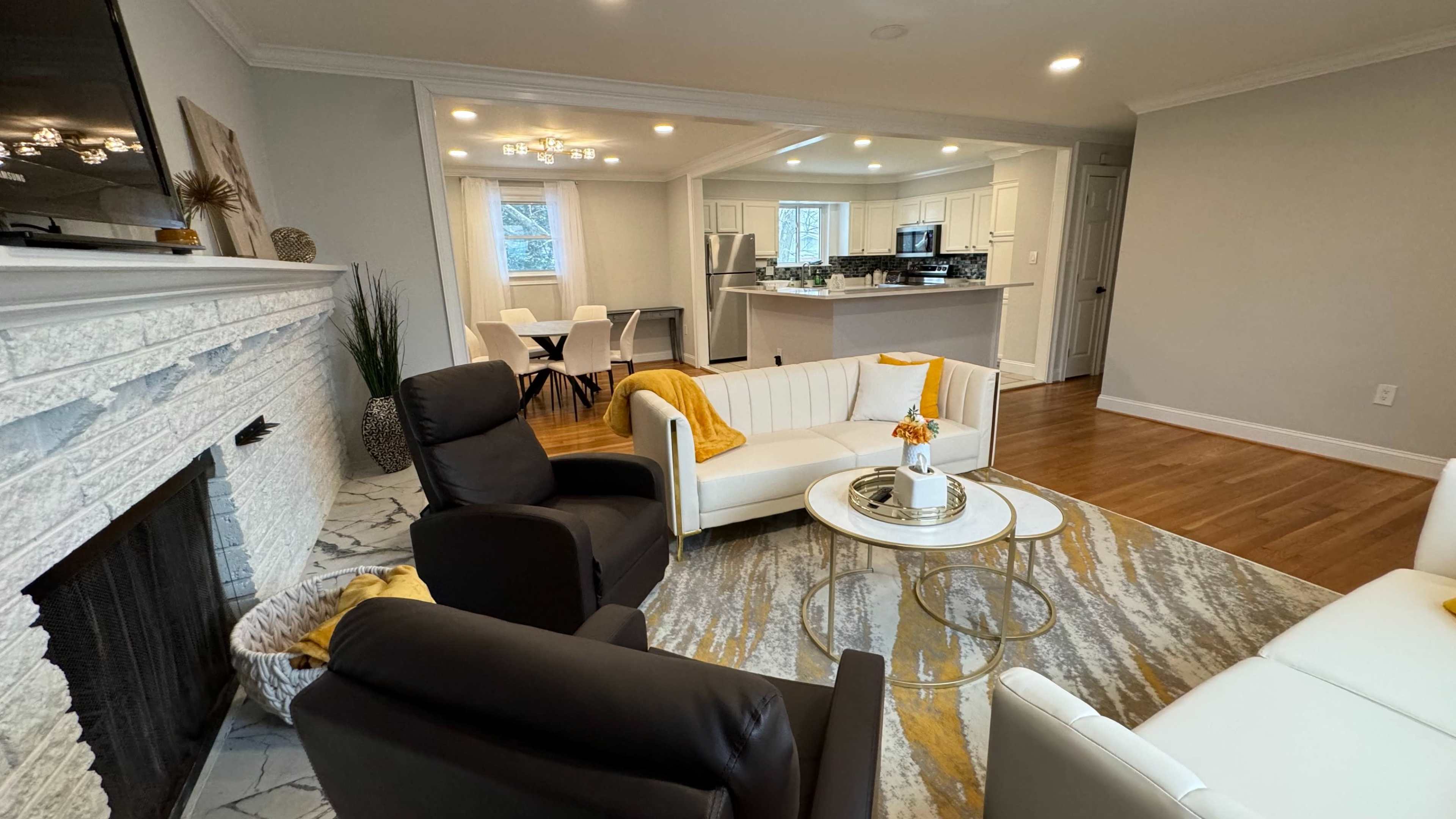 A modern living room featuring a white and black seating arrangement, a round coffee table, and an open kitchen area in the background.