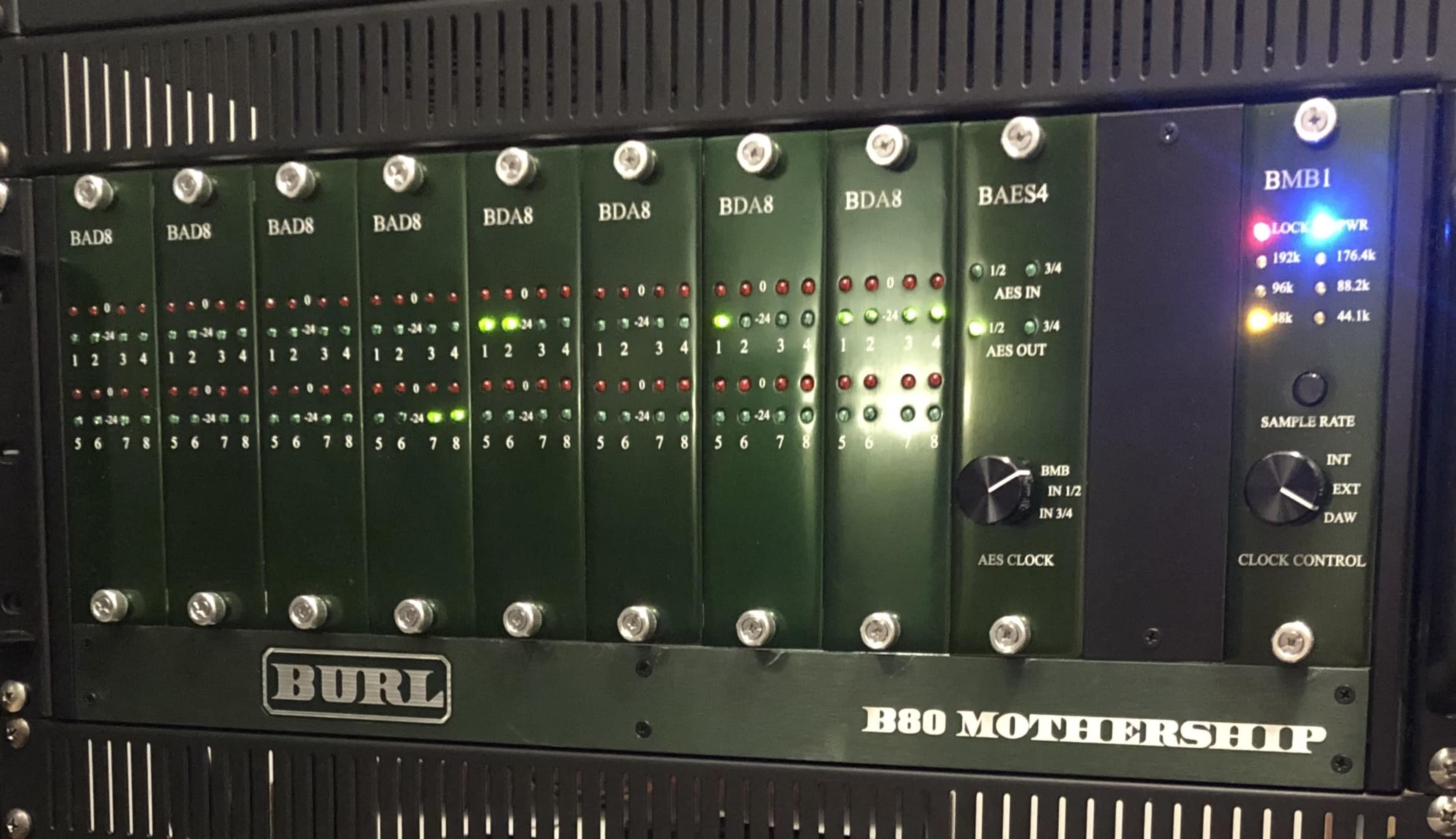 The image shows a rack-mounted audio interface with multiple channel inputs and output indicators, featuring various LED lights for monitoring status.
