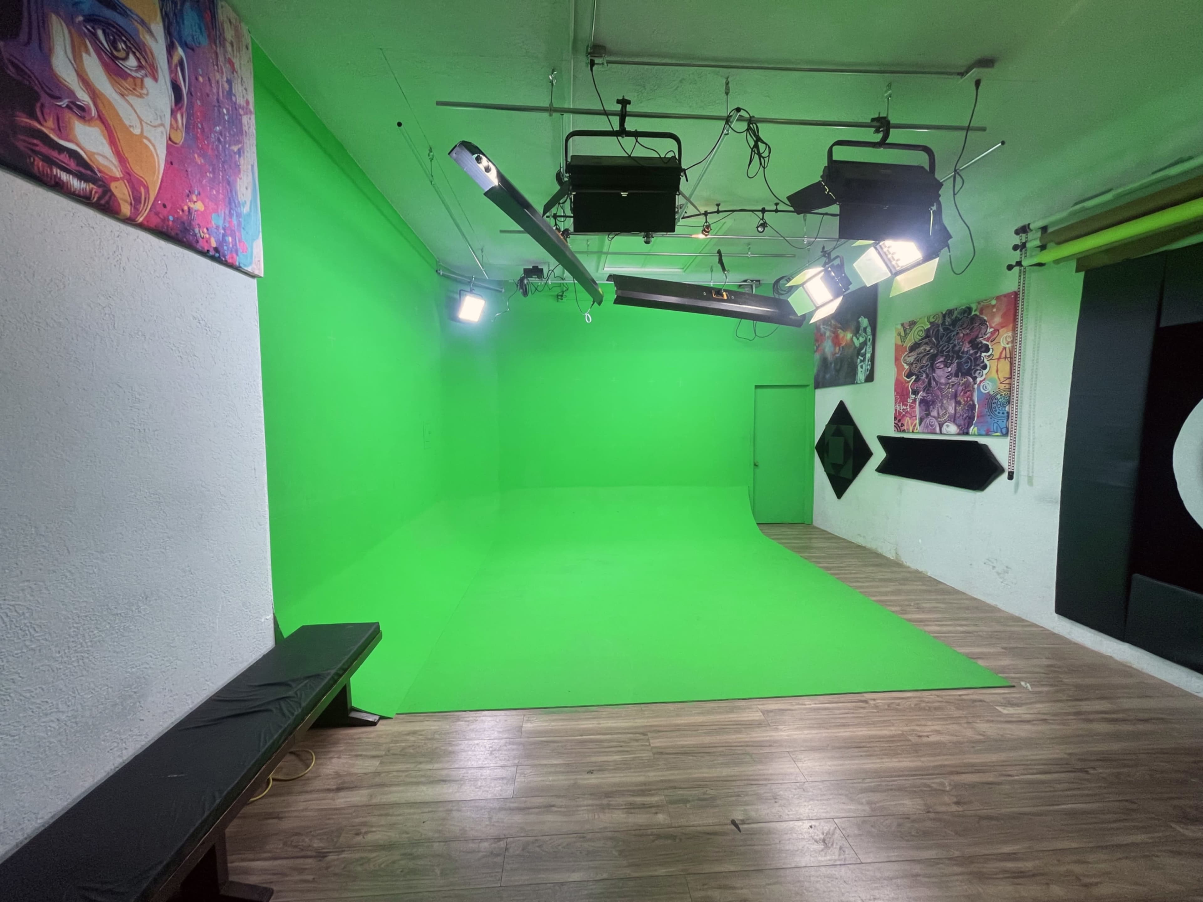 The image shows a green-screen studio with bright lights hanging from the ceiling and a wooden floor.